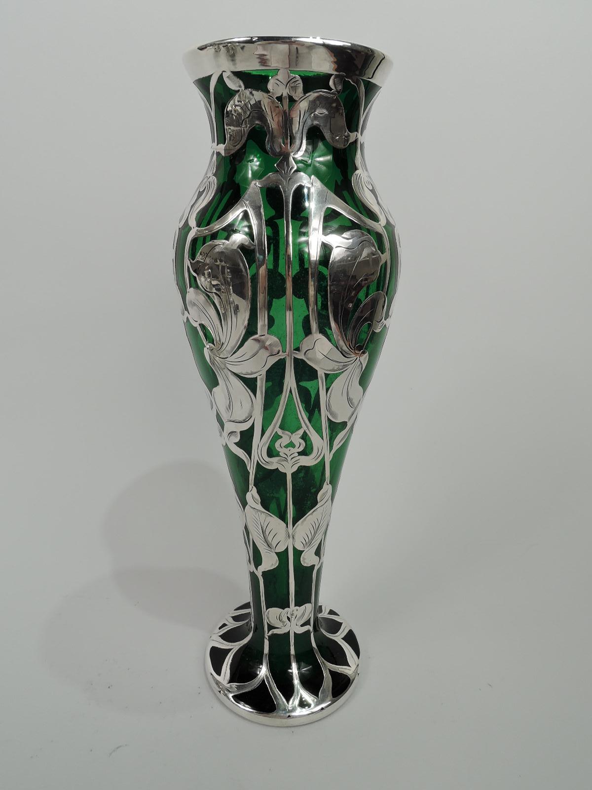 Turn-of-the-century American Art Nouveau glass vase with engraved silver overlay. Tall baluster flowing into round foot; flared mouth. Overlay in form of vertical pattern with loose blooms and curvilinear trellis-style tendrils that flow into