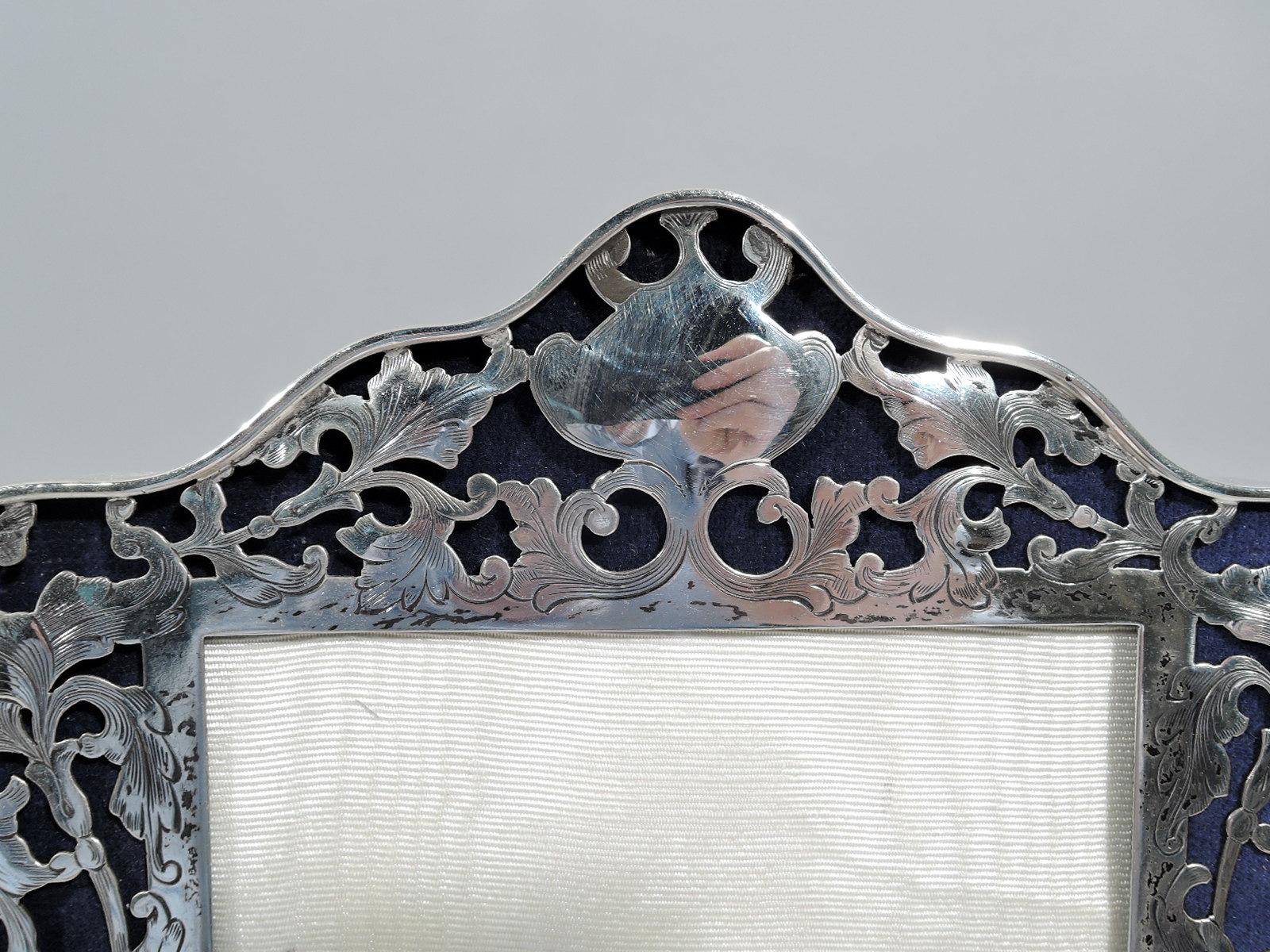 Art Nouveau sterling silver picture frame. Made by George A. Henckel & Co. in New York, ca 1910. Rectangular window in shaped surround with scrolled top and bottom and concave sides flowing into bracket supports. Front has pierced and engraved