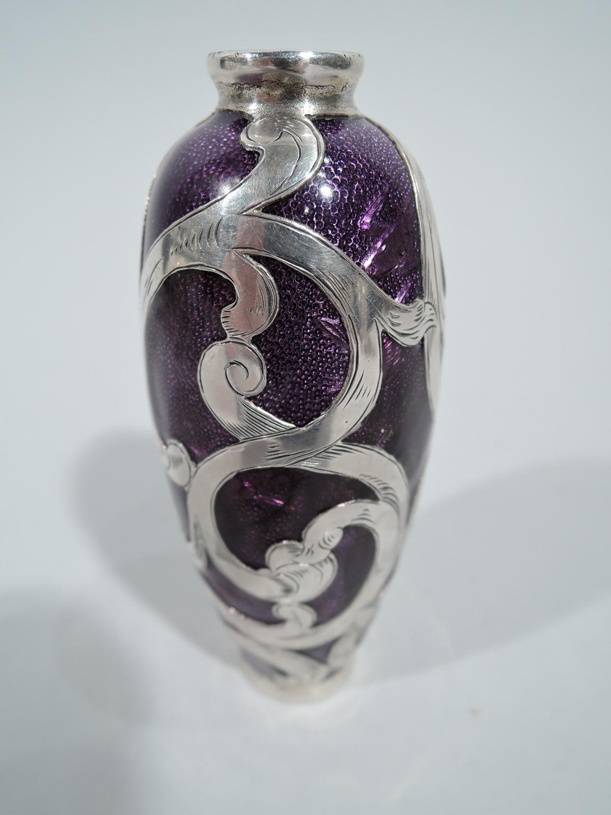 Turn-of-the-century American enamel bud vase with engraved silver overlay. Ovoid with foot ring and short neck in silver collars. Loose scroll overlay. Enamel is purple. Marked “Solid Silver”.