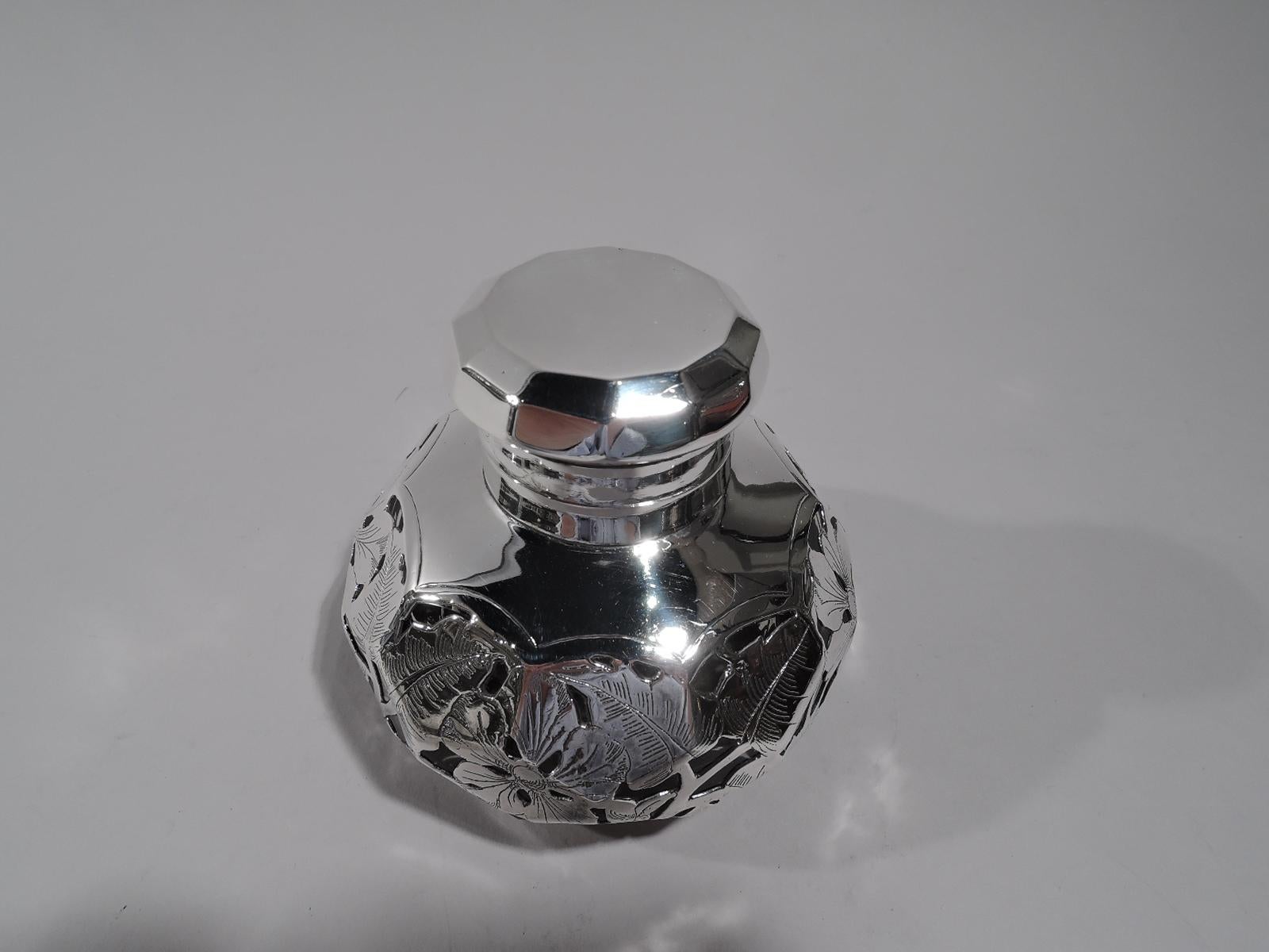 American Art Nouveau inkwell with engraved silver overlay, circa 1886. Bellied and faceted, short neck in silver collar and hinged and faceted silver cover. Overlay in form of dense and connected leafing and flowering branches. Glass is clear.