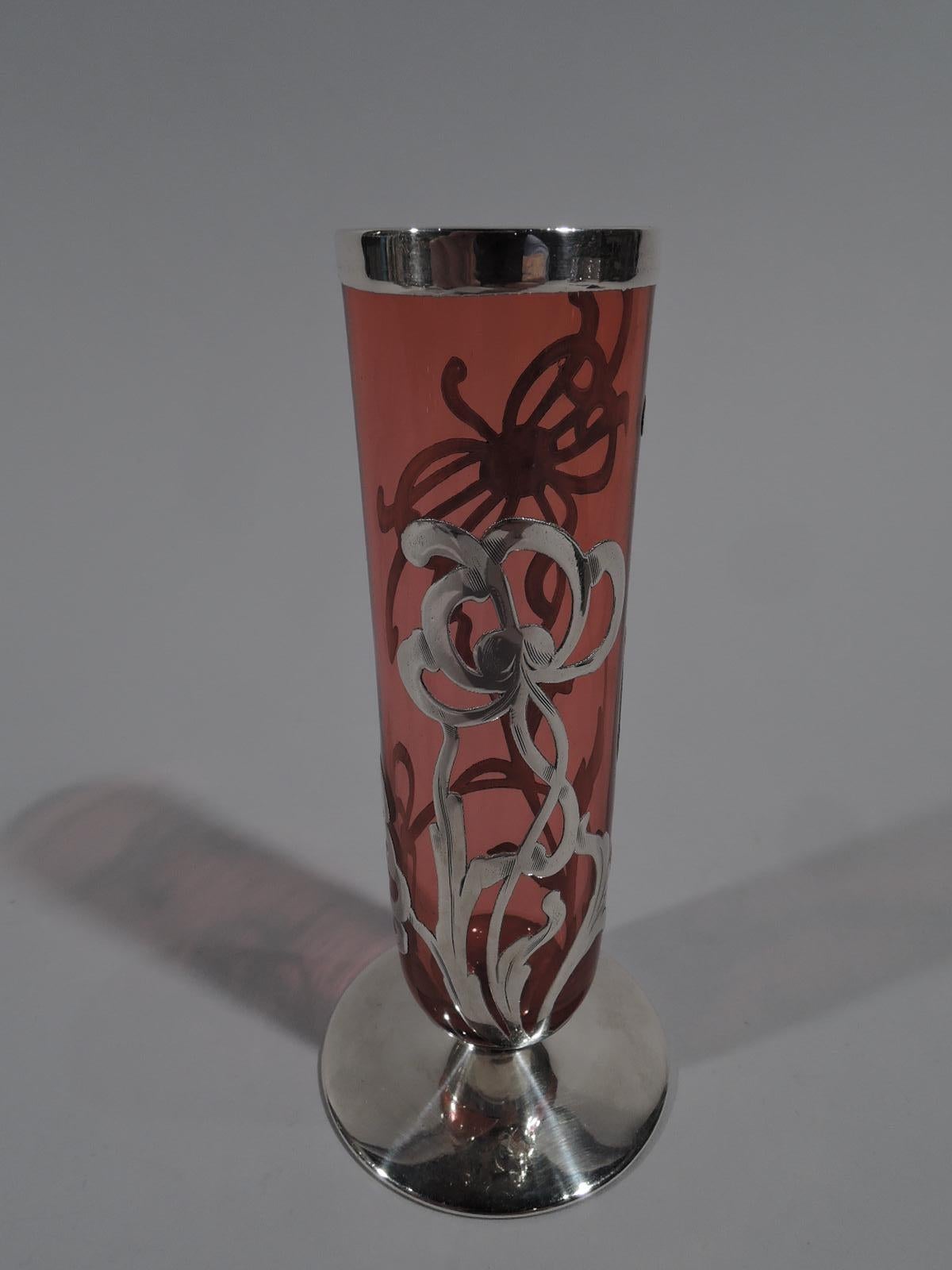 Turn-of-the-century American Art Nouveau glass bud vase with engraved silver overlay. Cylindrical with curved bottom and flat and round silver-covered foot. Open overlay in form of loose and spidery flowers. Glass is pinkish red.