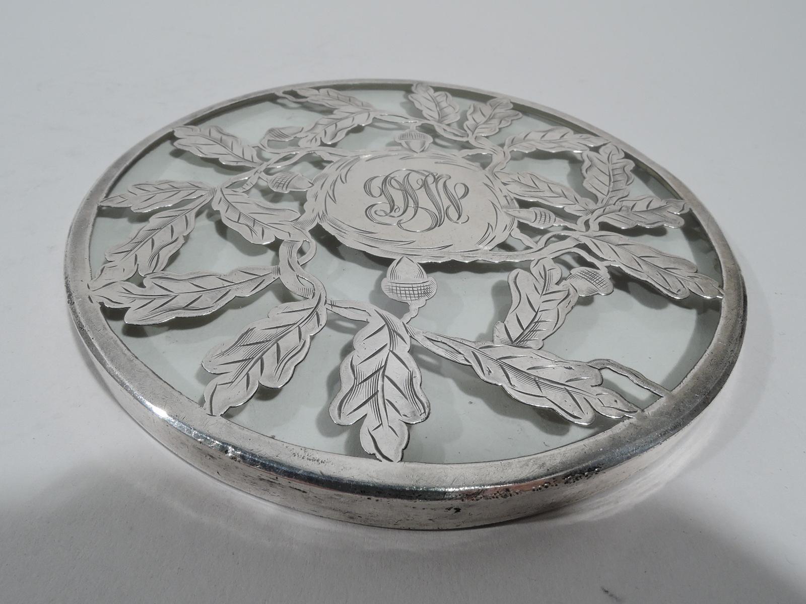 Turn-of-the-century American Art Nouveau glass trivet with engraved silver overlay. Leafing oak branch with acorns surrounding central round frame engraved with interlaced script monogram.
