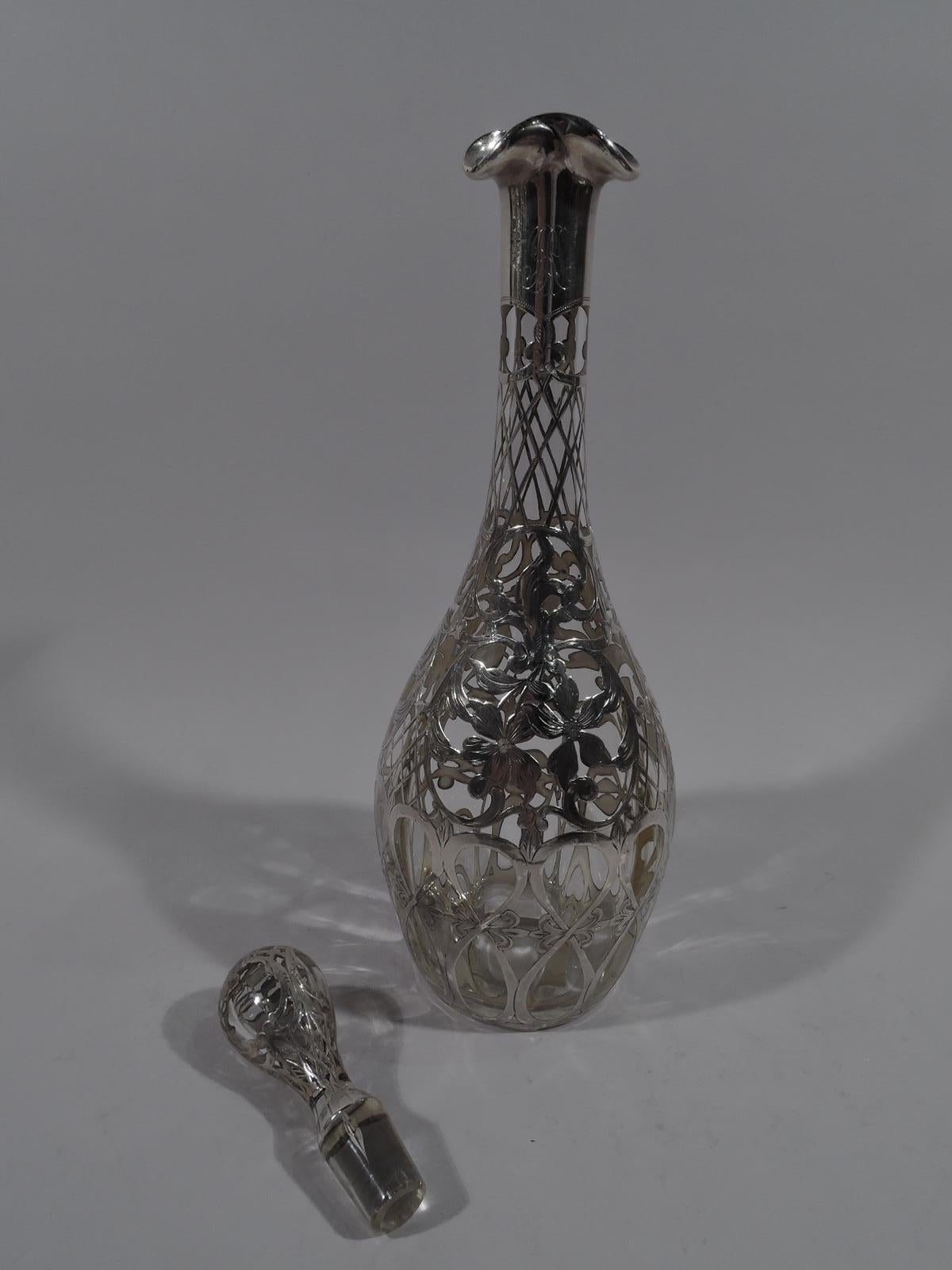 Turn of the century American Art Nouveau bottle decanter. Clear glass ovoid with tall cylindrical neck and ruffled rim. Ovoid stopper with short plug. Engraved silver overlay with loose flower heads surrounded by trellis; joined and elongated figure