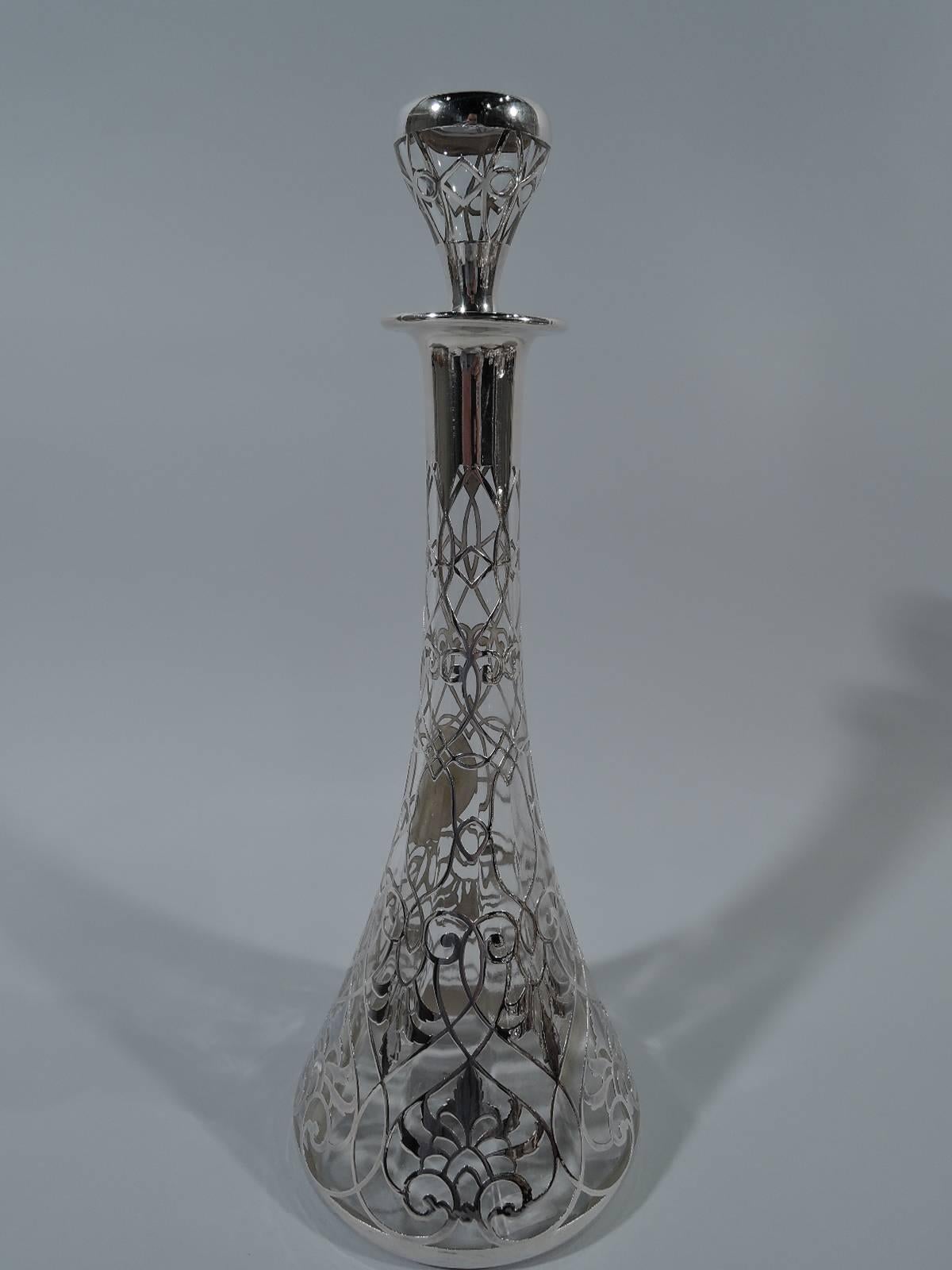 American Art Nouveau clear glass decanter with silver overlay. Conical. Fine overlaid ornament in form of vertical scrollwork with crisscrossing and threaded lines as well as stylized leaves. Neck top and everted rim in collar. Oval frame with