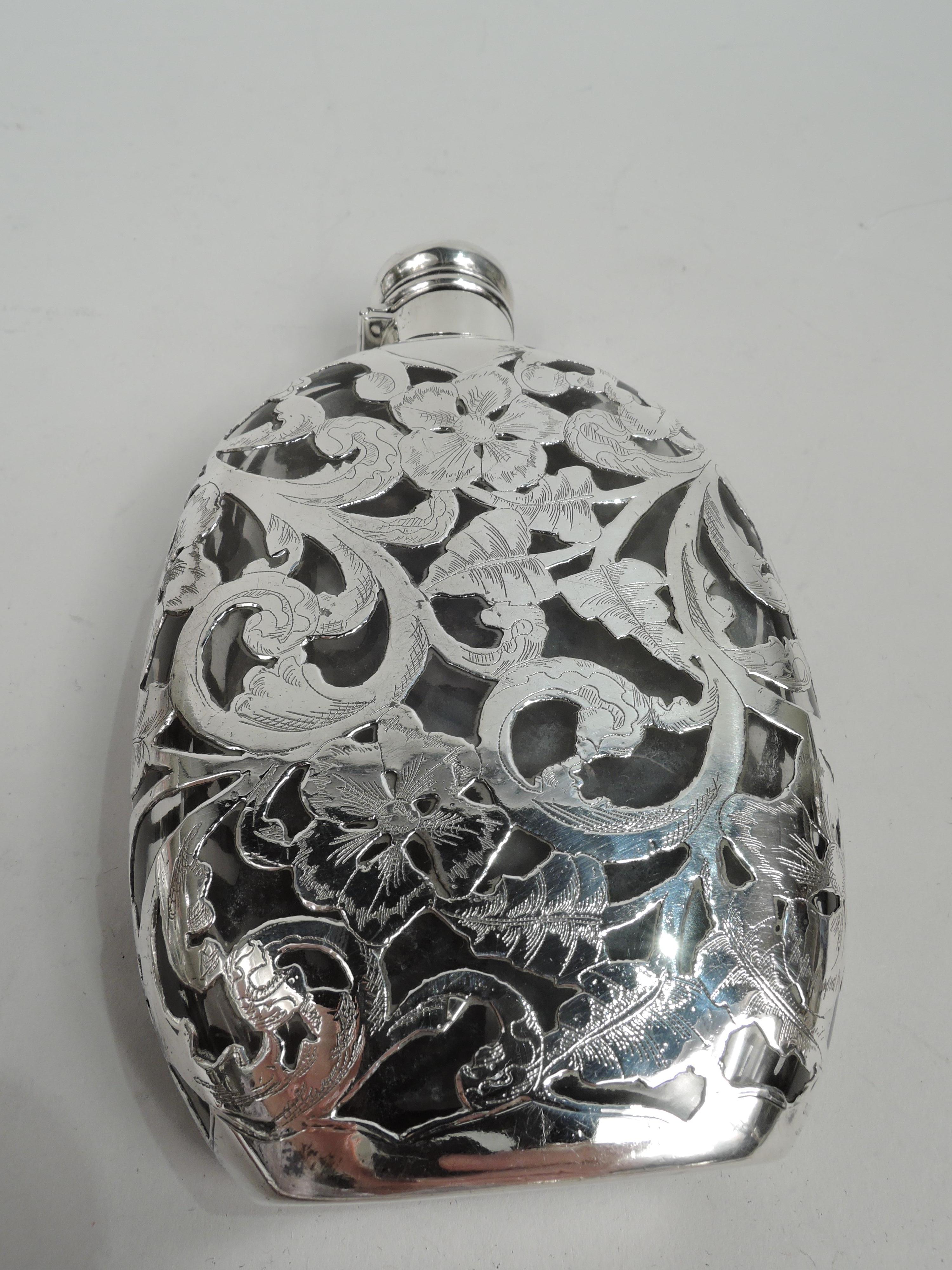 Turn-of-the-century American Art Nouveau glass flask with engraved silver overlay. Flat front and concave back; sides curved and bottom flat. Short neck in silver collar and hinged and cork-lined cover. Overlay in form of dense leafing scrollwork