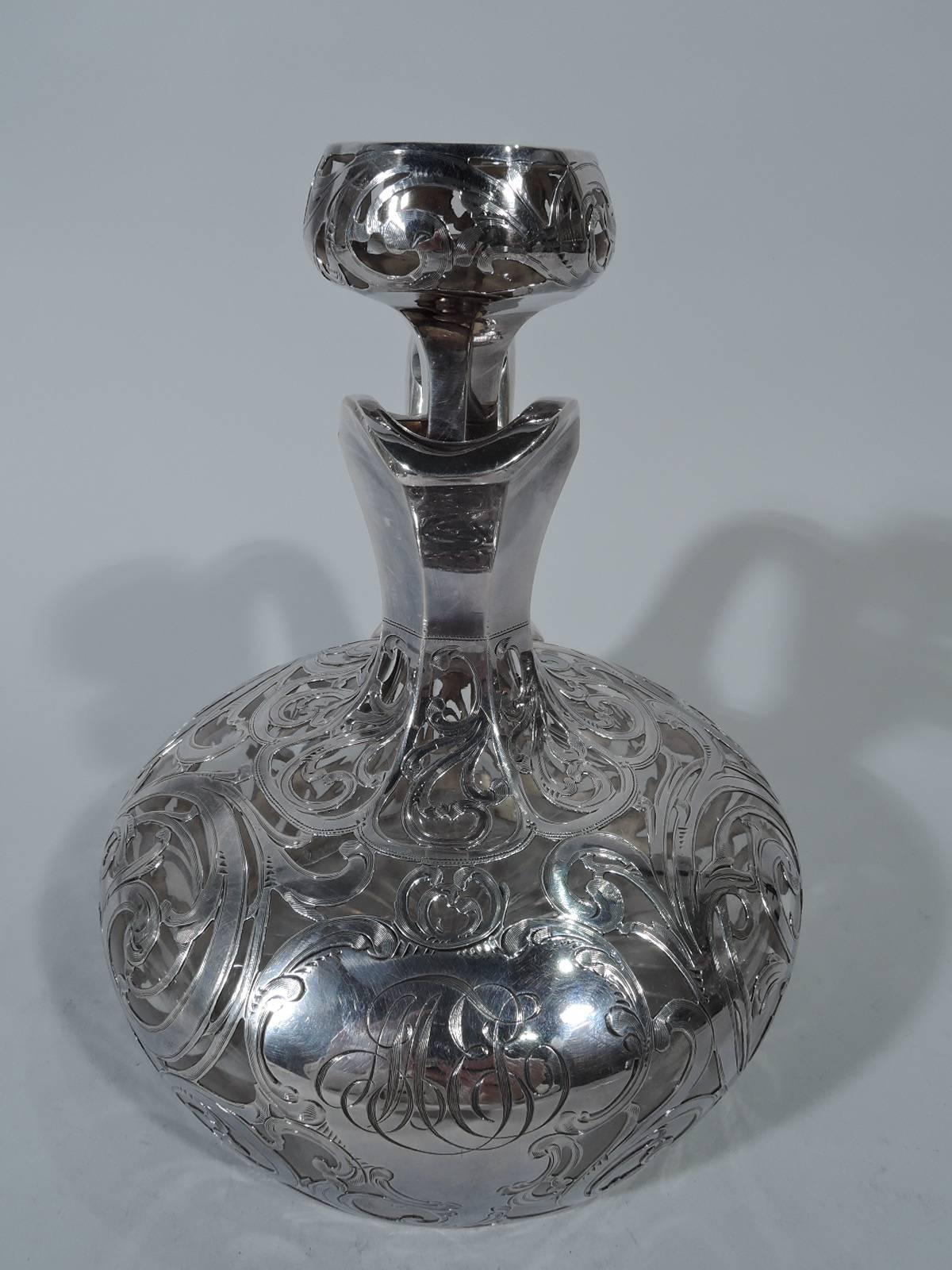 Art Nouveau clear glass jug decanter with silver overlay. Made by Alvin in Providence. Broad bellied bowl with faceted neck, helmet mouth, and high-looping scroll handle with flat thumb rest. Round flat-top stopper. Rinceaux overlay. Asymmetrical