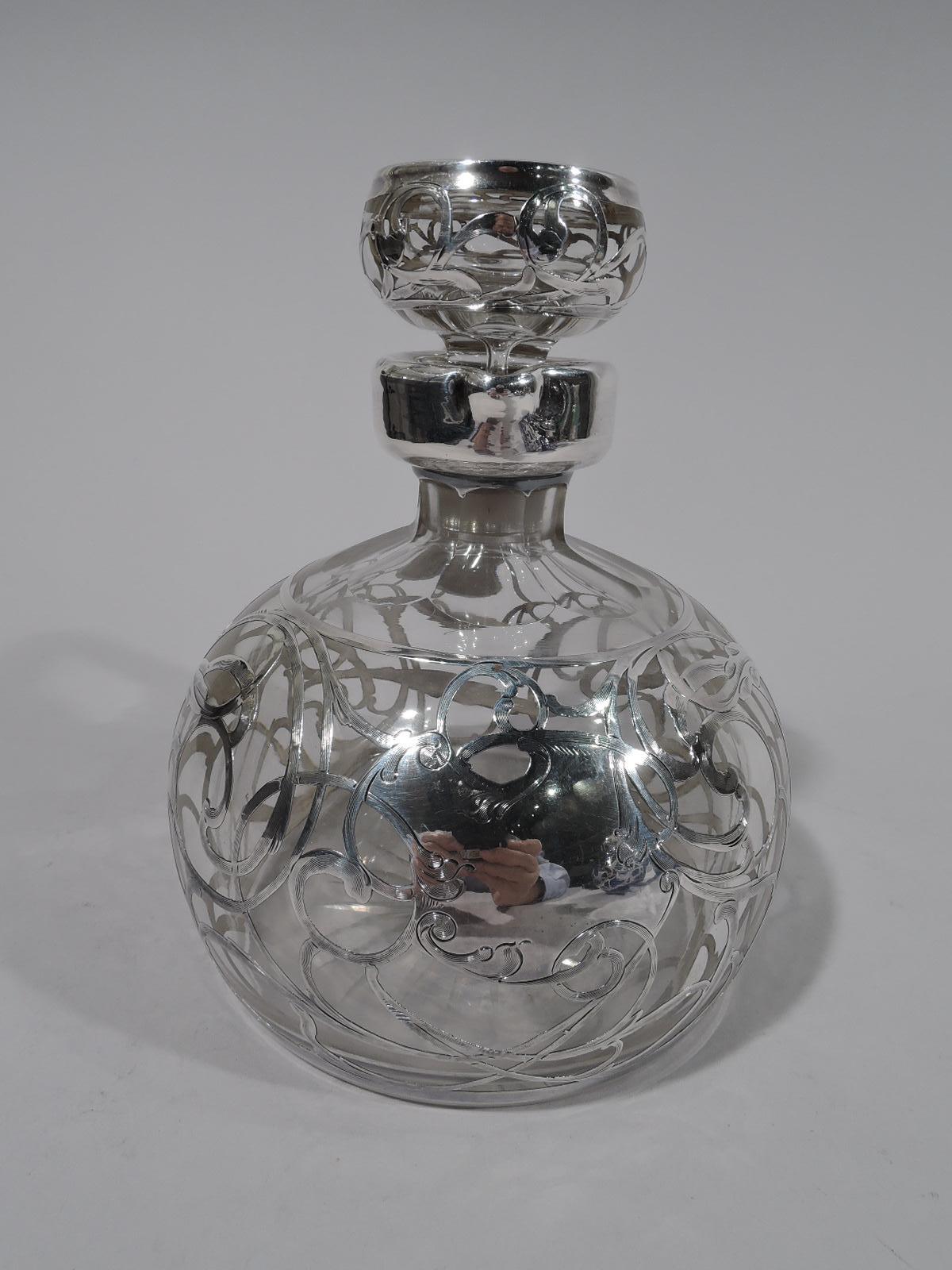 American Art Nouveau clear glass jug decanter with silver overlay, circa 1910. Globular with short faceted neck and bracket handle. Stopper flat topped with short plug. Rolling and entwined engraved silver scrollwork with leaves. Asymmetrical