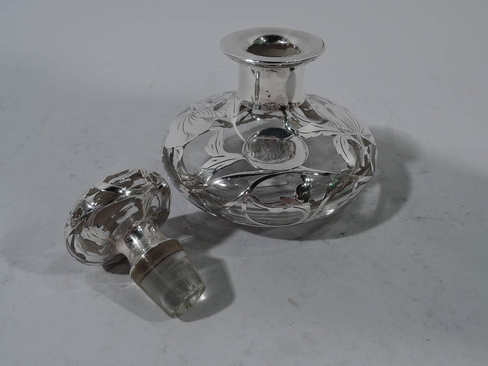 Art Nouveau clear glass perfume with silver overlay. Made by Matthews Company in Newark, circa 1910. Squat and bellied with short neck and everted rim in collar. Ornament in form of large and loose blooms with petals and stems. Overlay heightened