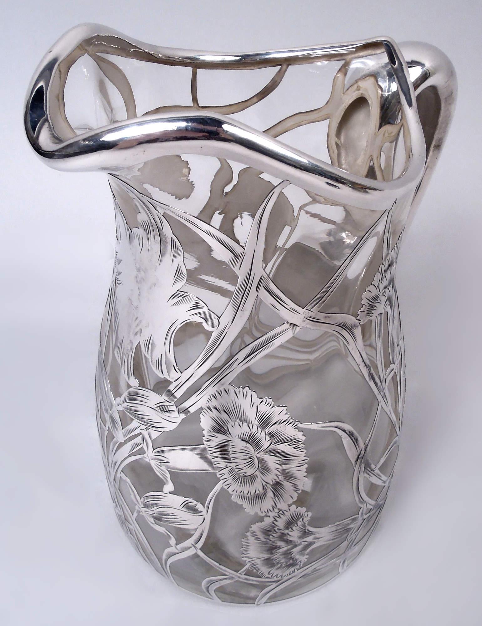 Jarra de agua de vidrio Art Nouveau americano con revestimiento de plata grabada, ca. 1900. Balaustre; boca ovoide con pico labial y asa en forma de c de plata. Superposición suelta y fluida con flores y capullos y zarcillos barridos por el viento.