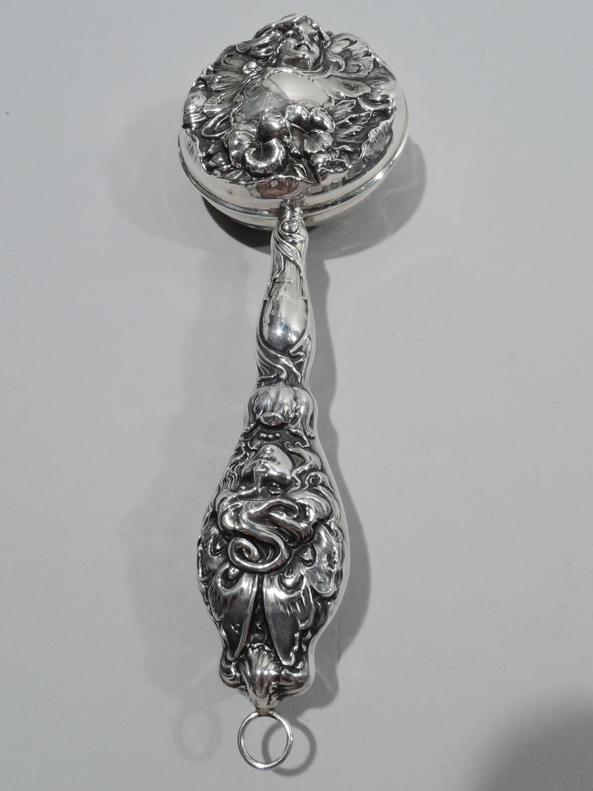 Turn-of-the-century American Art Nouveau sterling silver rattle. Round head and baluster handle with embossed ornament: Female heads with fairy wings and tresses flowing into scrolls and flowers. Scrolled cartouches (vacant). Marked “Sterling” and