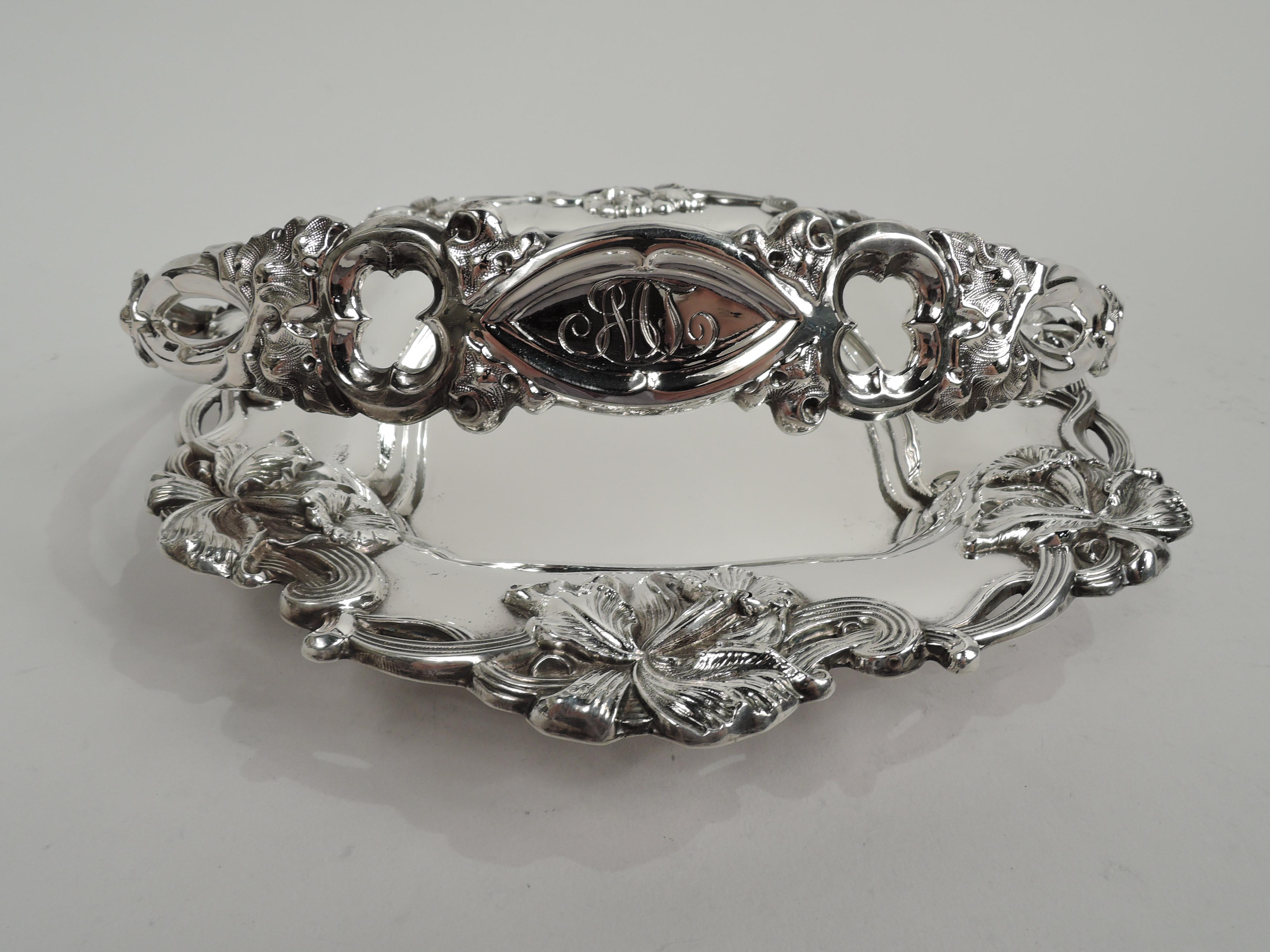 Art Nouveau sterling silver basket. Rectangular shaped well. Rim open and applied with entwined and reeded stems and loose and fluid flower heads. C-scroll swing handle with alternating open shapes, stippled leaves, and central solid oval cartouche