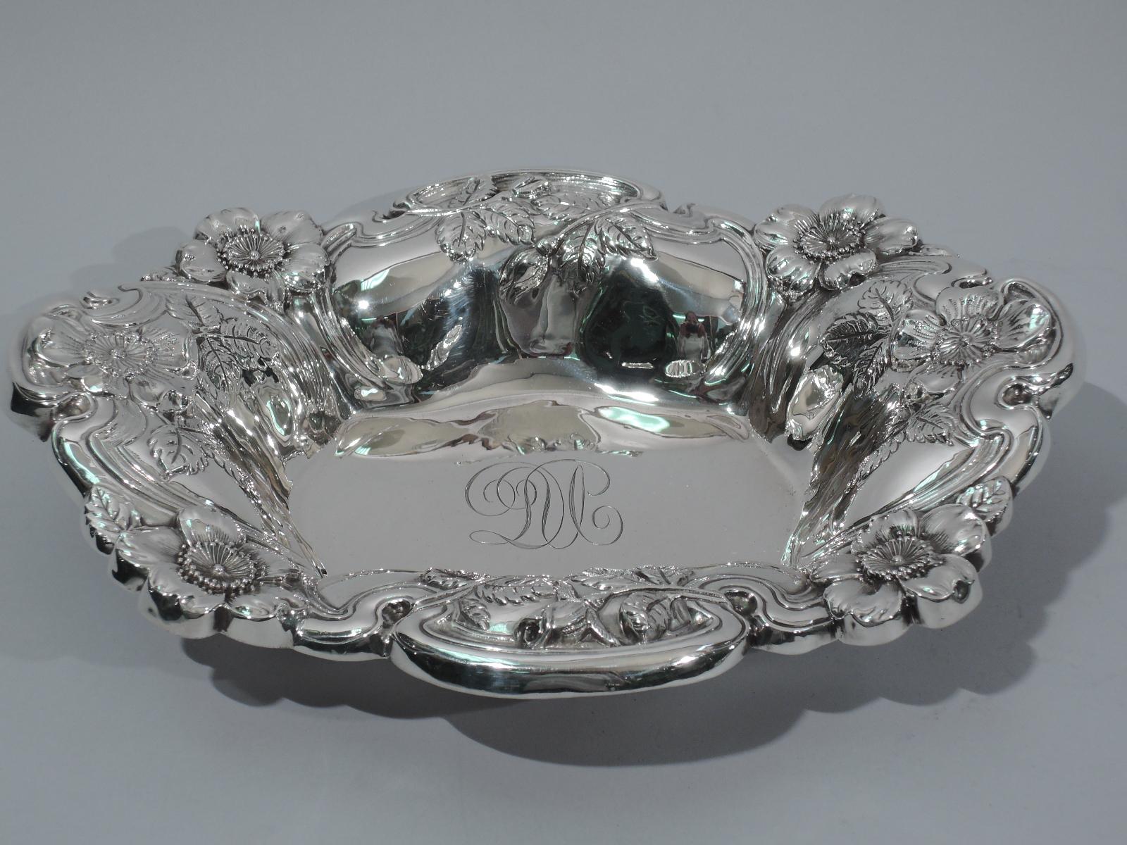 Turn-of-the-century American Art Nouveau sterling silver bowl. Scrolled and rectilinear well. Sides lobed and flared with irregular scrolled rim. Chased ornament comprising flowerheads overlapping whiplash frames. Interlaced script monogram engraved