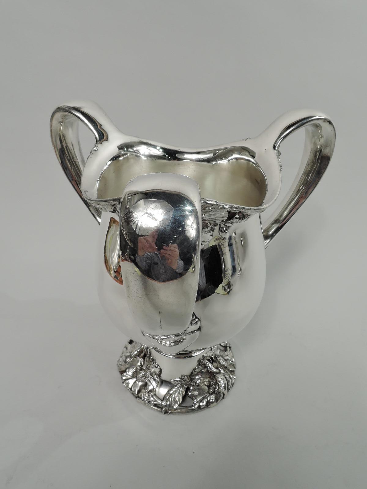 Turn-of-the-century Art Nouveau sterling silver loving cup. Made by Frank W. Smith in Gardner, Mass. Curved body with 3 high-looping handles and domed foot. Flower heads clustered at rim under handles. Foot same with openwork. Fresh and voluptuous