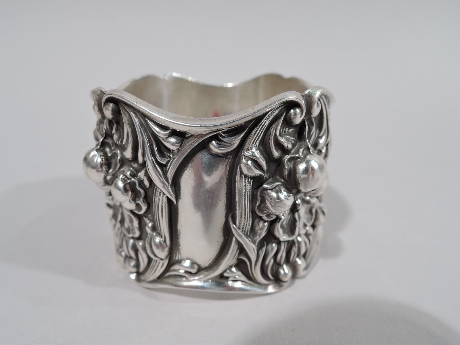Turn of the century Art Nouveau sterling silver napkin ring. Wavy rims. Chased and tooled ornament with blossoms set in scrolled and reeded frames. Dense and textural with alternating vacant scrolls. Fully marked including Webster maker’s stamp.