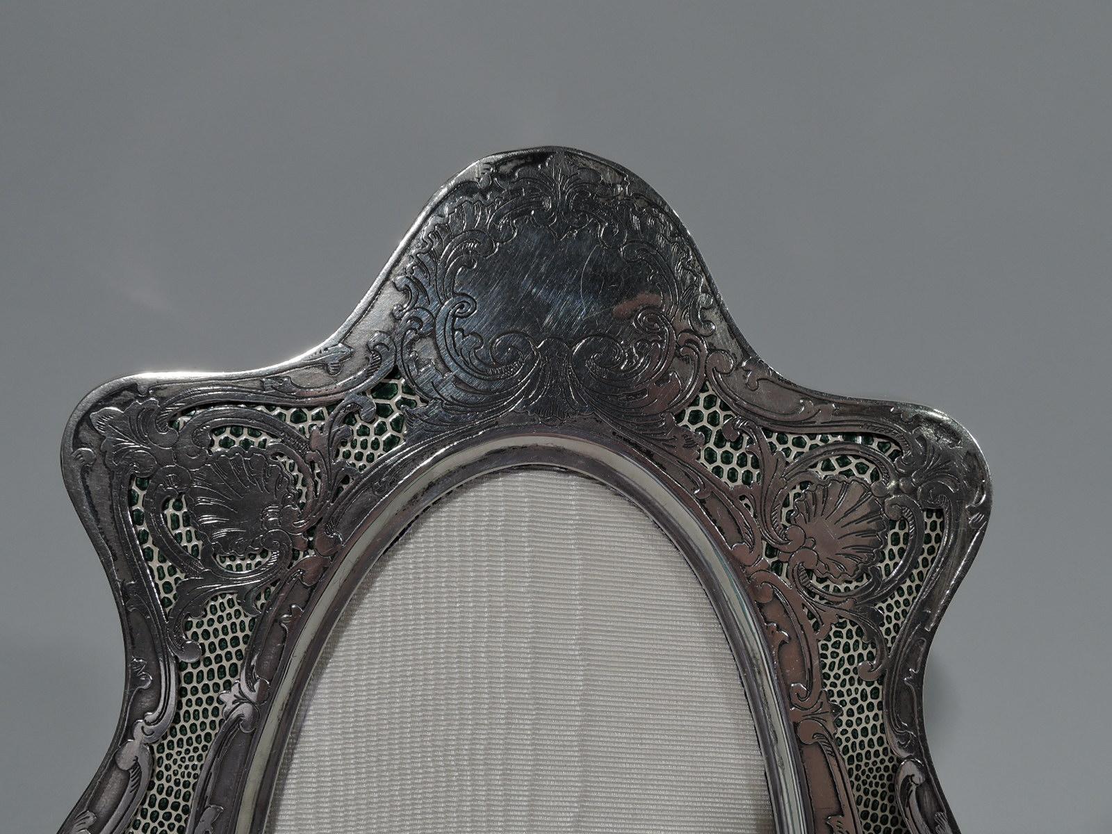 American Art Nouveau sterling silver picture frame, circa 1900. Narrow oval window in wavy-shaped surround with bracket feet. Open ornament with leaves, flowers, and shells on irregularly speckled green and white ground. Top solid with scrolled