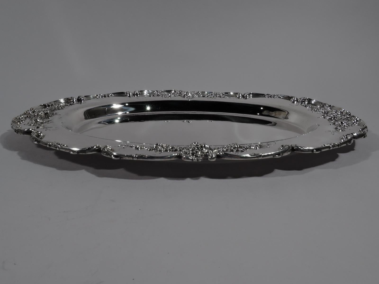 Turn-of-the-century American Art Nouveau sterling silver tray. Deep and oval well. Wide shoulder with applied floral garlands. Scalloped rim with applied c-scrolls. Tactile with nice heft. Fully marked including retailer’s stamp for JB Hudson & Son