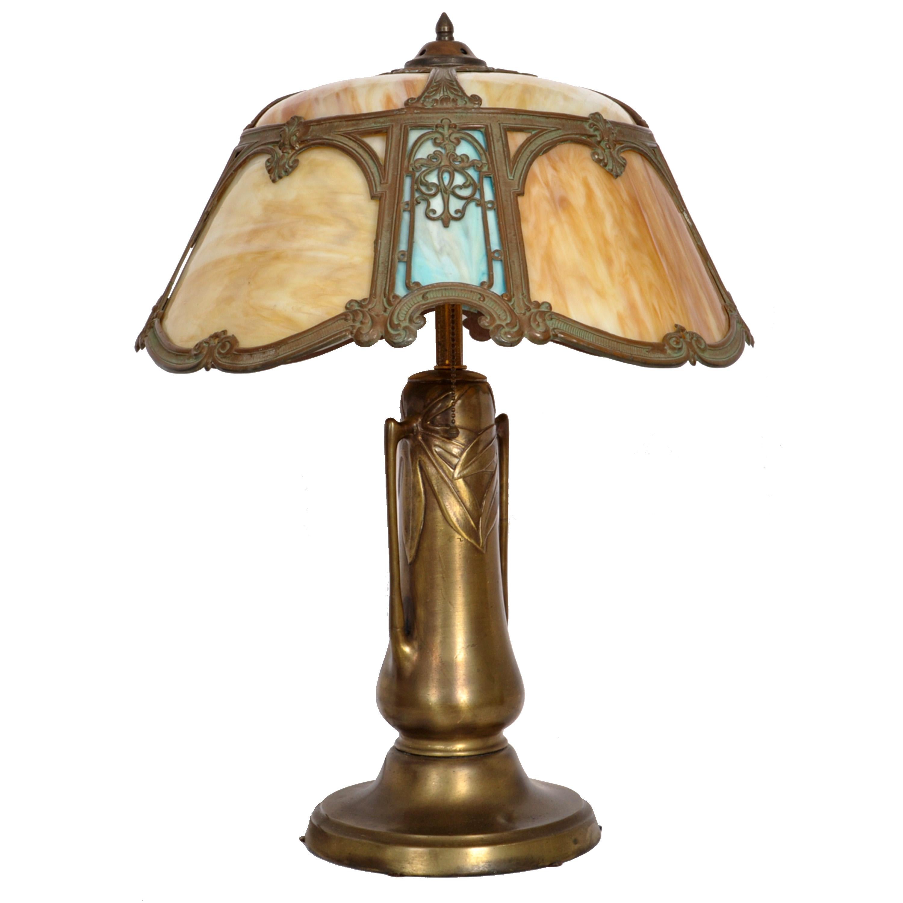 A good and unusual antique American Art Nouveau/ Craftsman/ Mission bronze and slag glass lamp, Circa 1910.
The twin light lamp having a helmet shaped shade with filigree work and is inset with striated caramel and blue slag glass panels.
The gilded