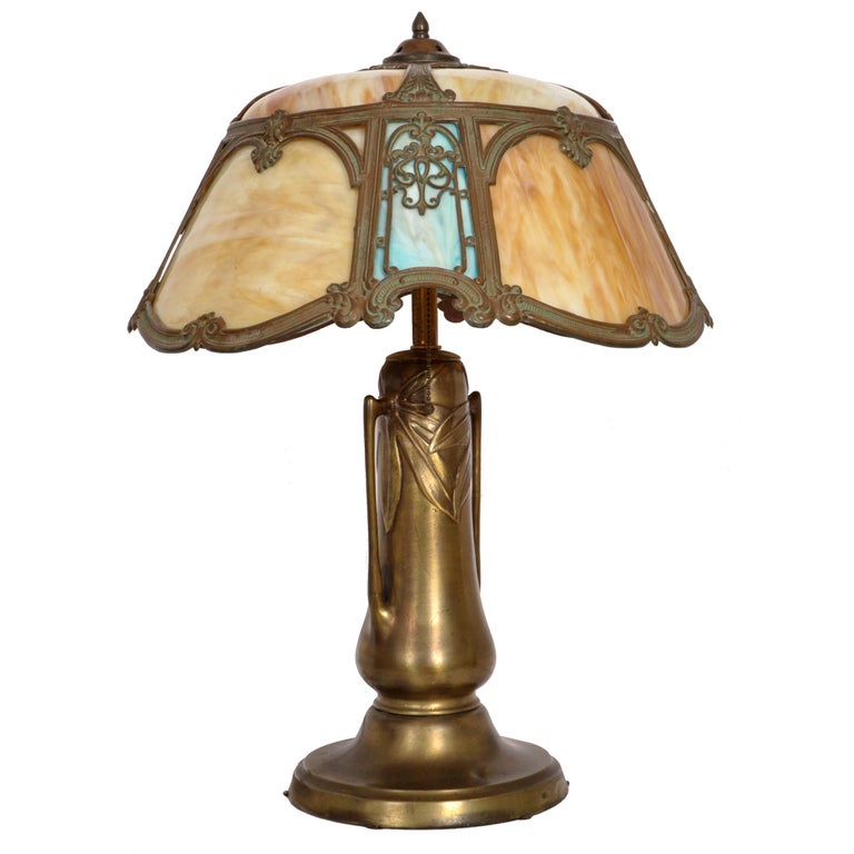 A good and unusual antique American bronze and slag glass lamp, Circa 1910.
The twin light lamp having a helmet shaped shade with filigree work and is inset with striated caramel and blue slag glass panels.
The gilded base having twin handles and