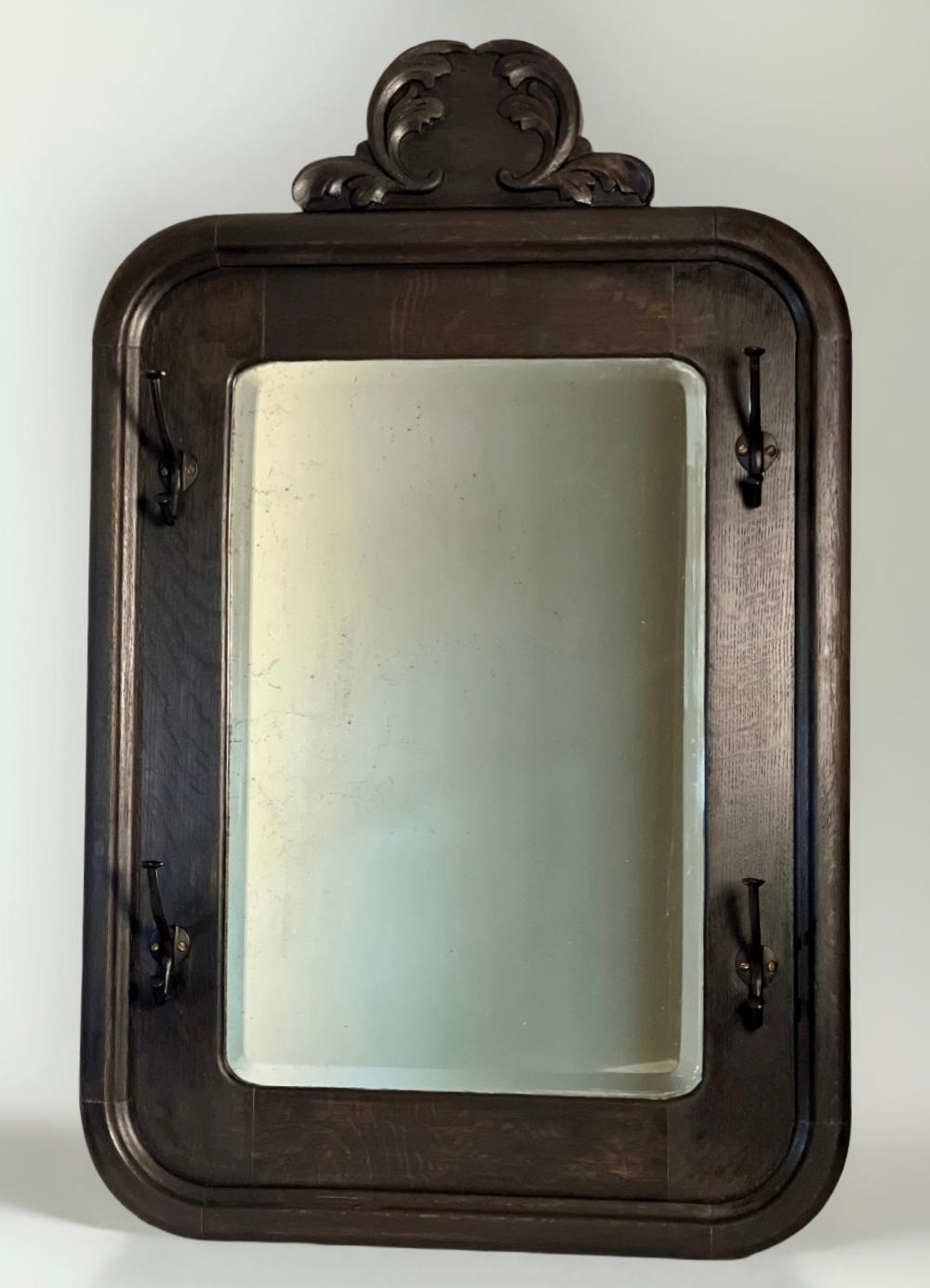 Wonderful Arts and Crafts period American carved oak hanging wall coat/hat rack with a large beveled mirror, refinished in black stain, circa 1910. The robust frame features four double iron hooks, a rounded rectangular trim with a bullnose edge and