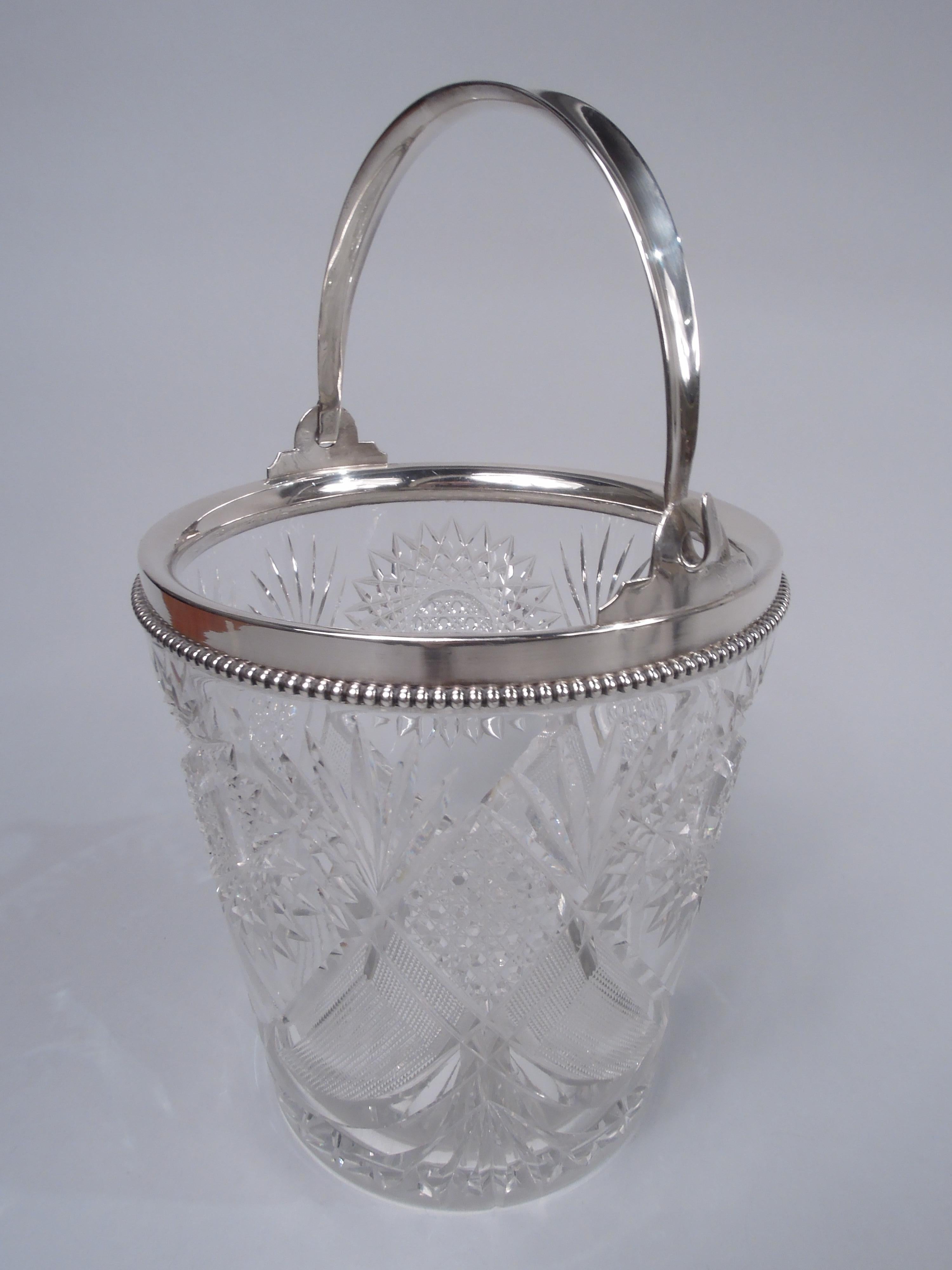 Victorian brilliant-cut glass ice bucket with sterling silver mounts. Made by Wilcox (part of International) in Meriden, Conn., ca 1900. Tapering sides with diaper and star ornament. Mouth has sterling silver collar with beaded rim and c-scroll
