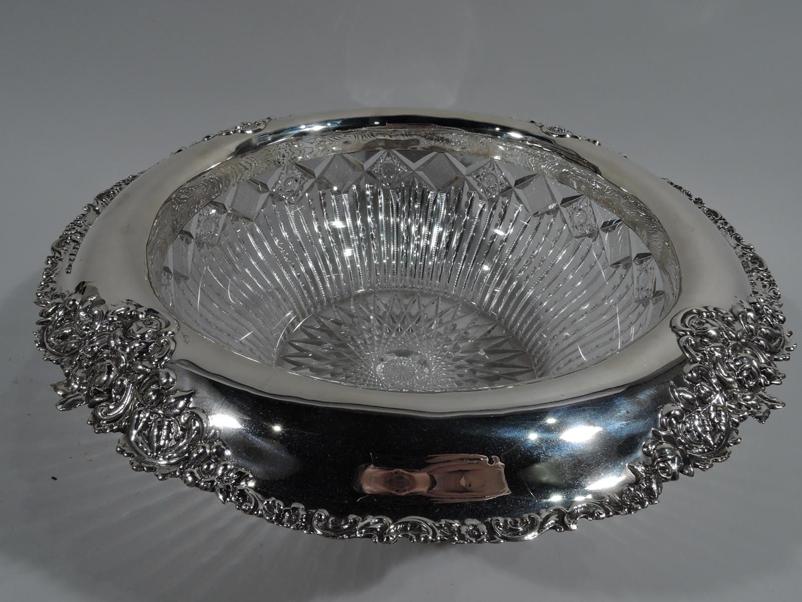 American brilliant-cut glass punch bowl with sterling silver collar, circa 1900. Bowl has curved sides with diaper border over flutes and notches. Star on underside. Turned-down and scrolled rim with applied flower bunches. Indistinct maker’s mark