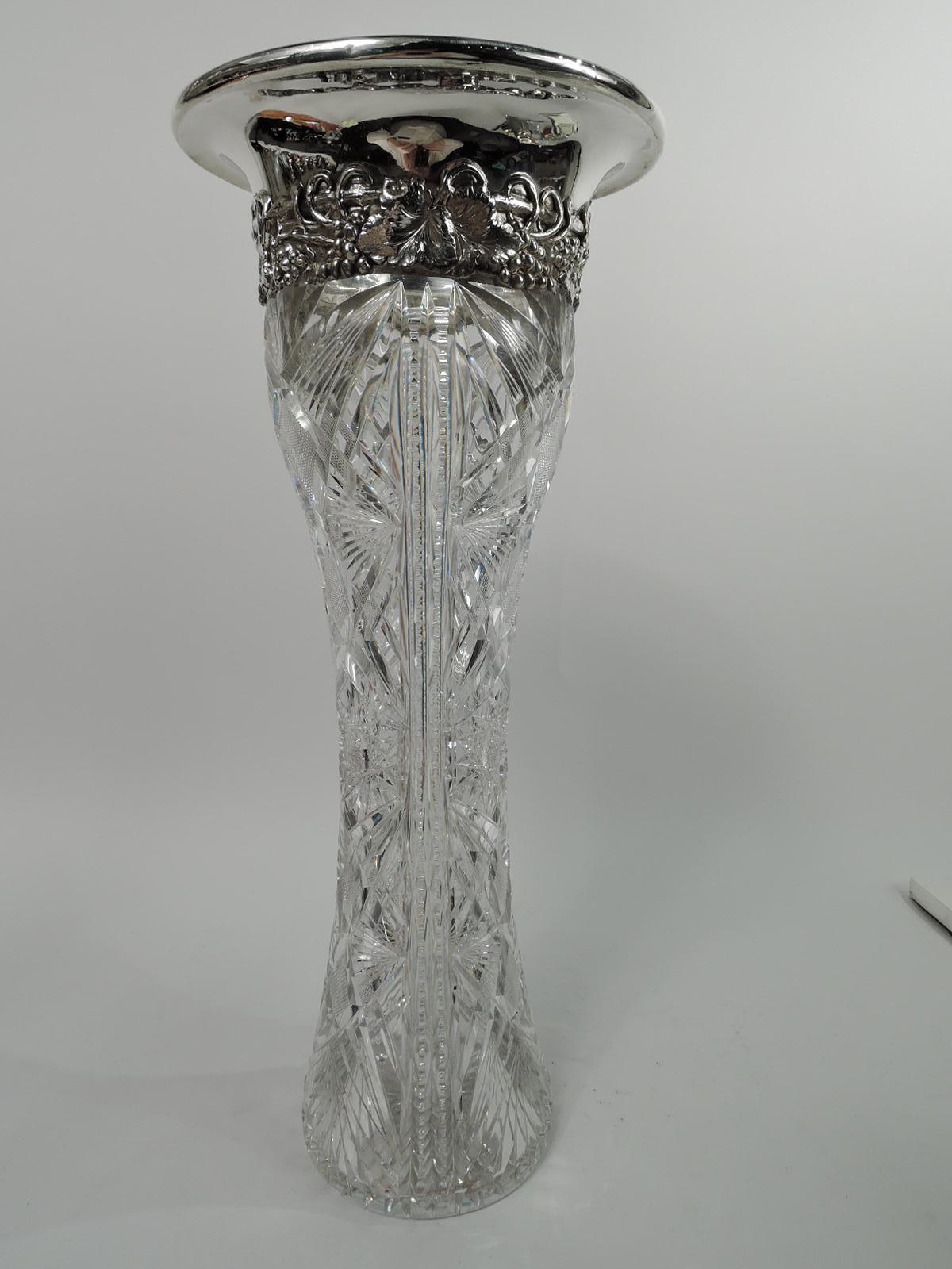 Turn-of-the-century brilliant-cut glass and sterling silver vase. Made by J. F. Fradley & Co. in New York. Tall and waisted cylinder with ferns, stars, and diaper between double notched vertical borders. Sterling silver collar with applied fruiting