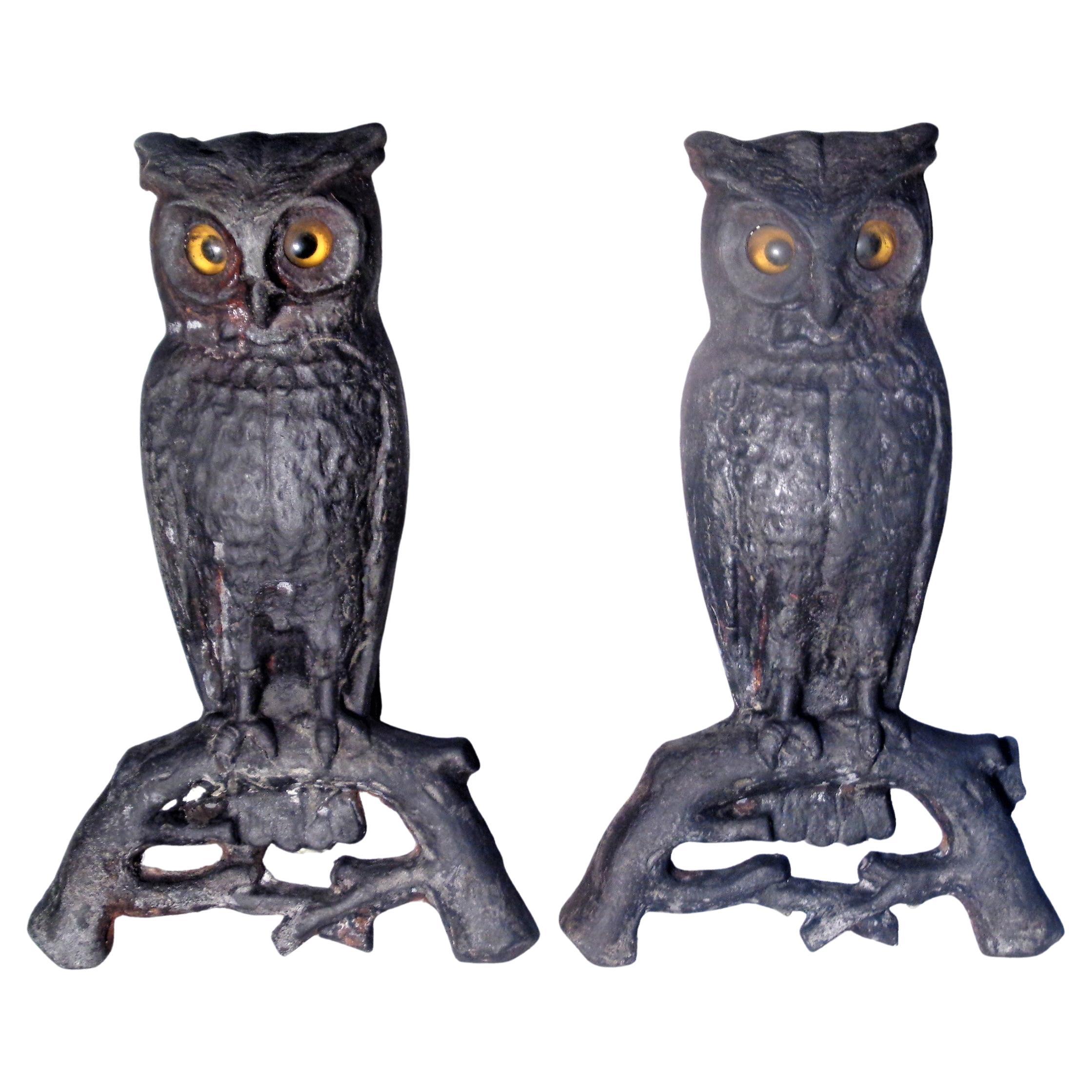 Pair of antique American cast iron owl andirons with the original amber yellow and black glass eyes. Overall nicely aged old blackened surface. Circa 1890-1900. Owls perched upright on tree branches measure 15