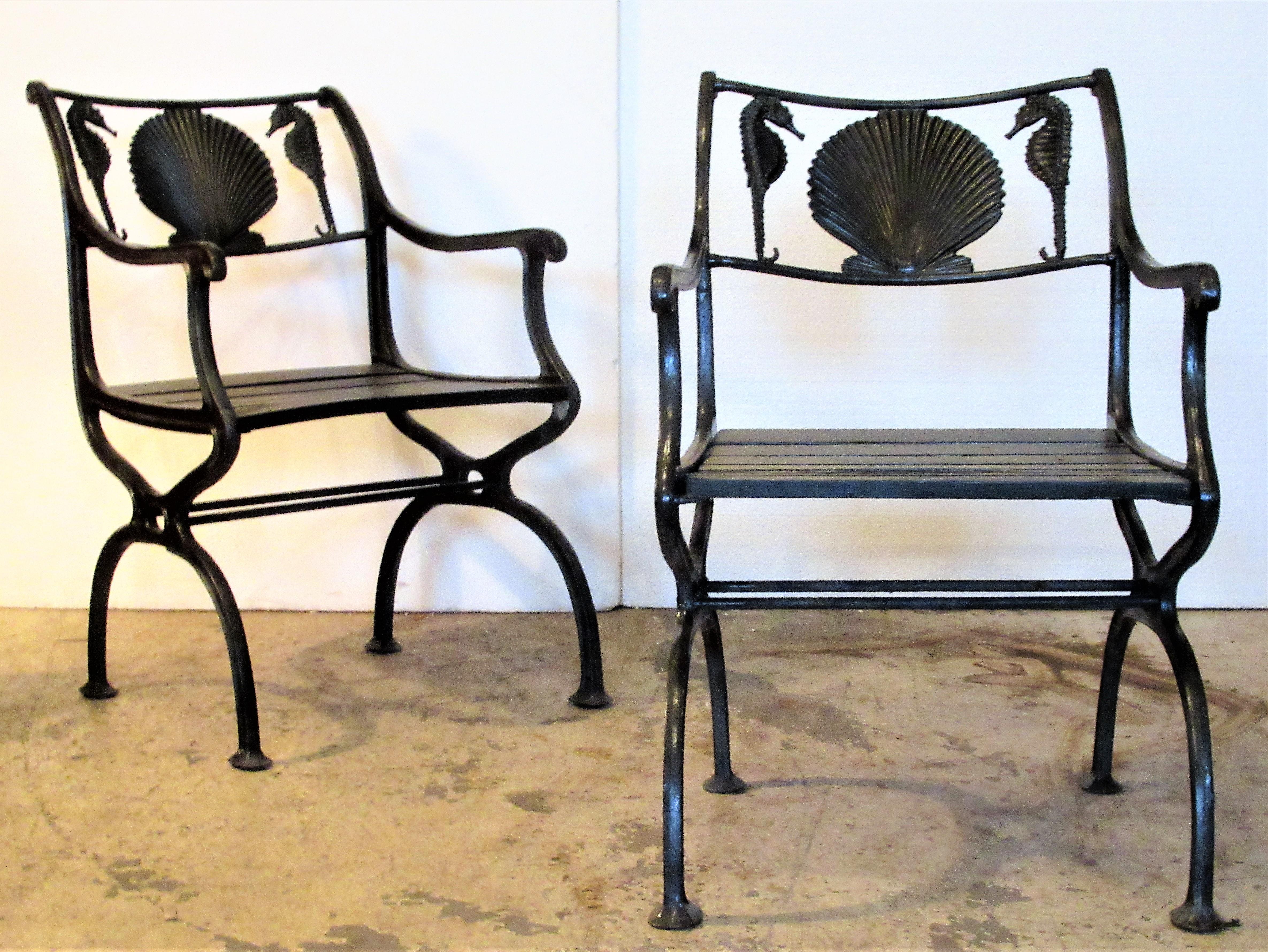 Pair of antique American black painted cast iron garden chairs with curved arms, wood plank seats and finely detailed sea horse and scallop shell design at top rails. They are stamped in iron at upper side seat rail Marcy Foundry - NY, NY patent