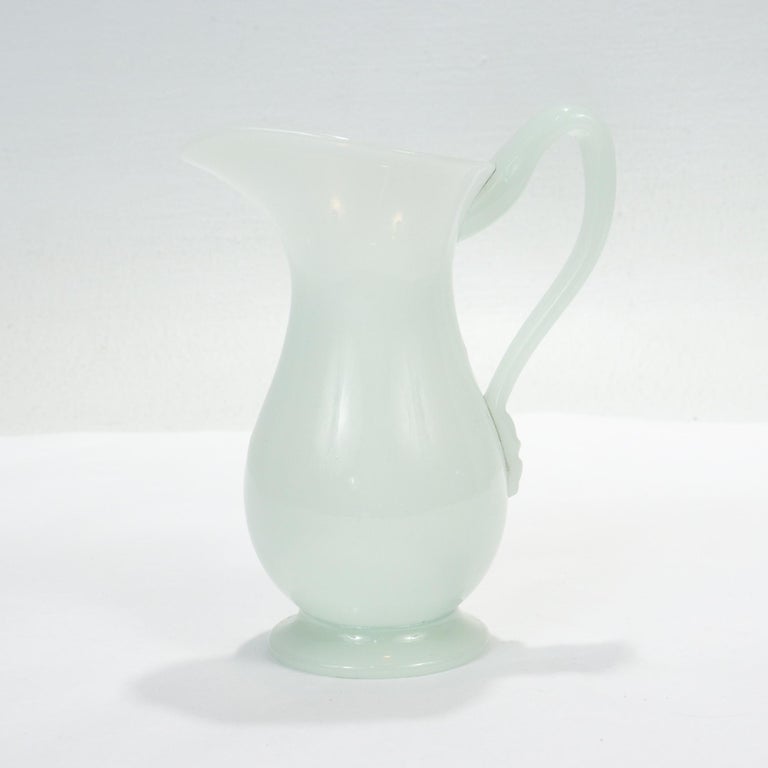 A fine antique handblown glass jug or miniature pitcher.

In an opaque clam broth glass with an applied handle and foot.

We are unsure if this is a South Jersey cream pitcher (and/or some American glass house production) or whether this small