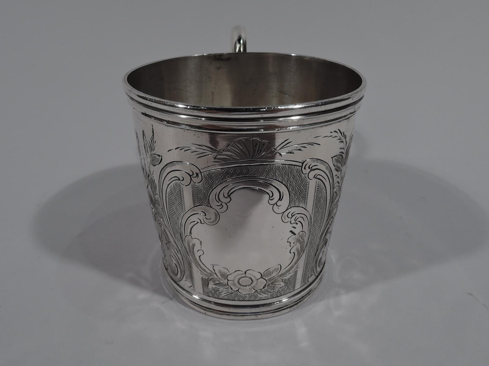 American classical coin silver baby cup, circa 1850. Drum-form with molded rim and base, and S-scroll handle. Engraved scrolled frames with leafy-scrolls and scallop shells, of which 2 filled with engine-turned ornament, and 1 inset with scrolled