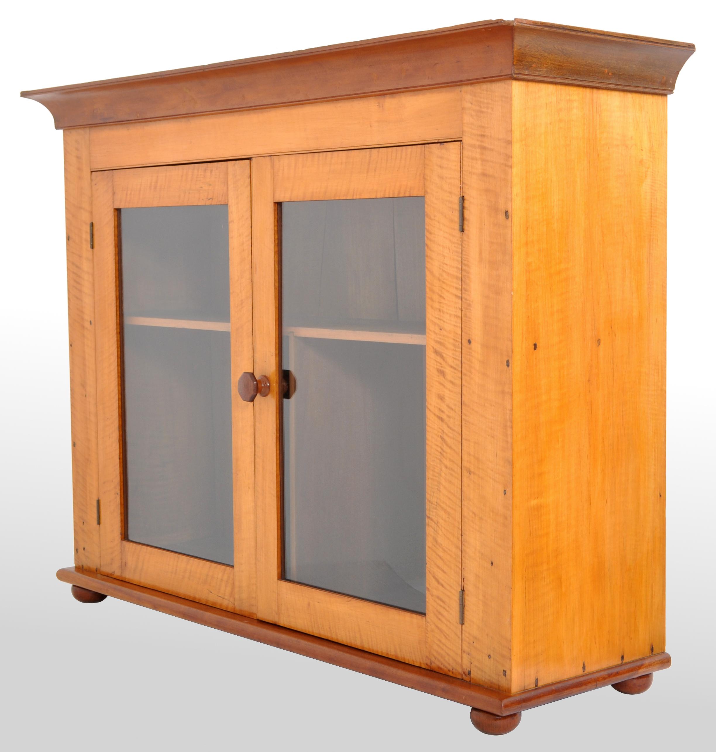 Antique American Country 'Tiger' maple twin door cabinet, Pennsylvania, circa 1840. The top having a flared cornice below two glazed doors enclosing a single shelf, standing on small compressed bun feet. A good pre-civil war American cabinet in