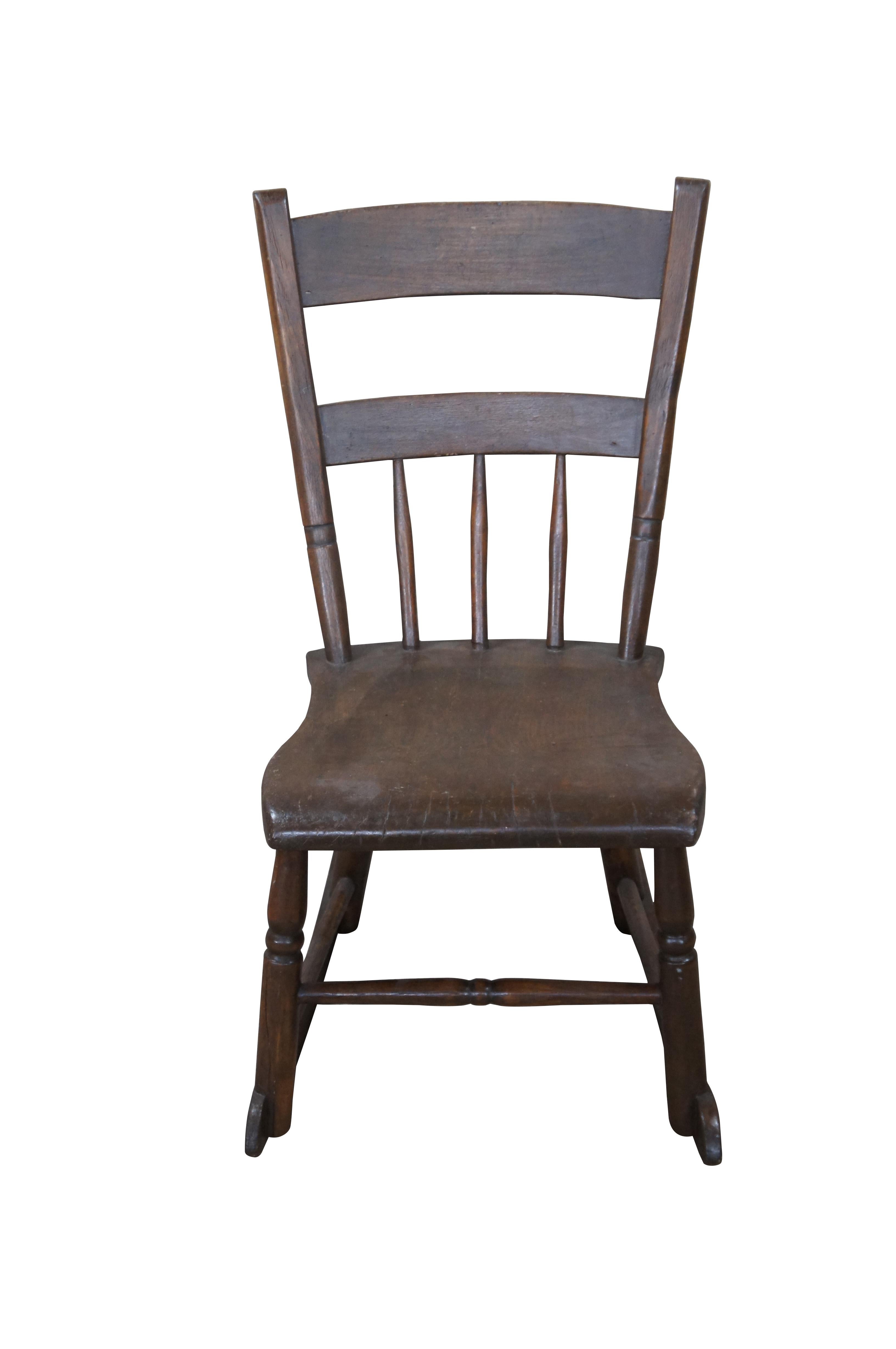 Early 20th Century American Country Rocking Chair.  Made from oak with a ladder form and spindles.  Features a contoured seat over short supports leading to rockers.  

Dimensions:
26.5