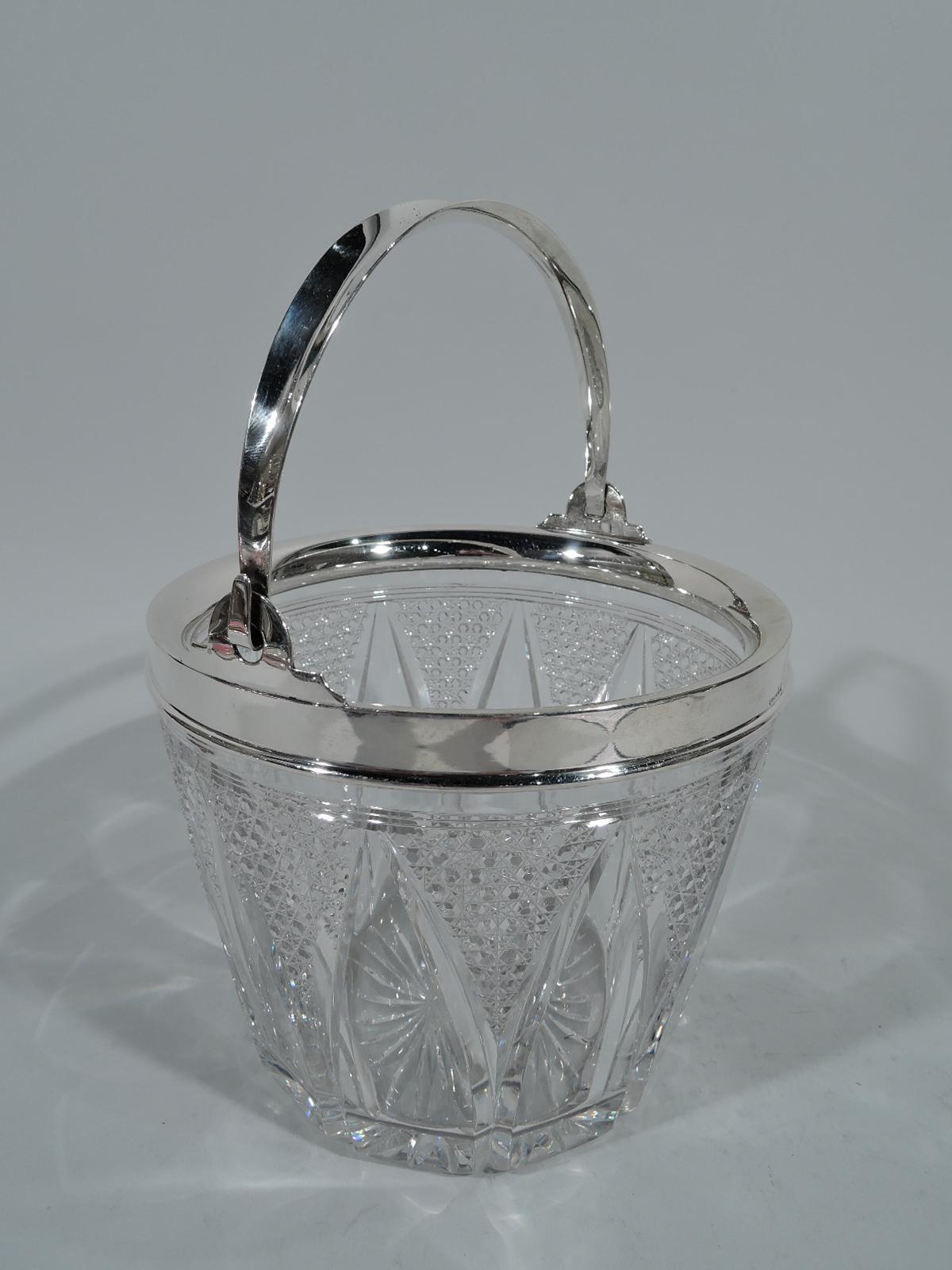 Turn-of-the-century cut glass and sterling silver ice bucket. Made by Wilcox Silver Plate Co. (a division of International) in Meriden, Conn. Round clear glass with band of stylized leaves, and diaper triangles with facets and starts. Sterling