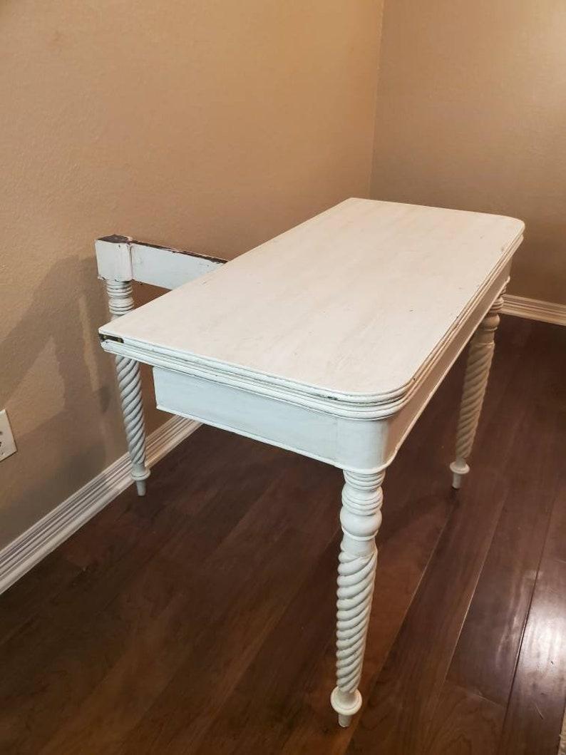 A 19th century American morphing table, in a later white painted finish. Having a demilune (half-moon console / side table) shaped hinged fold-over top, rising on hand turned and spiral twist legs, flip the top open to extend into a circular