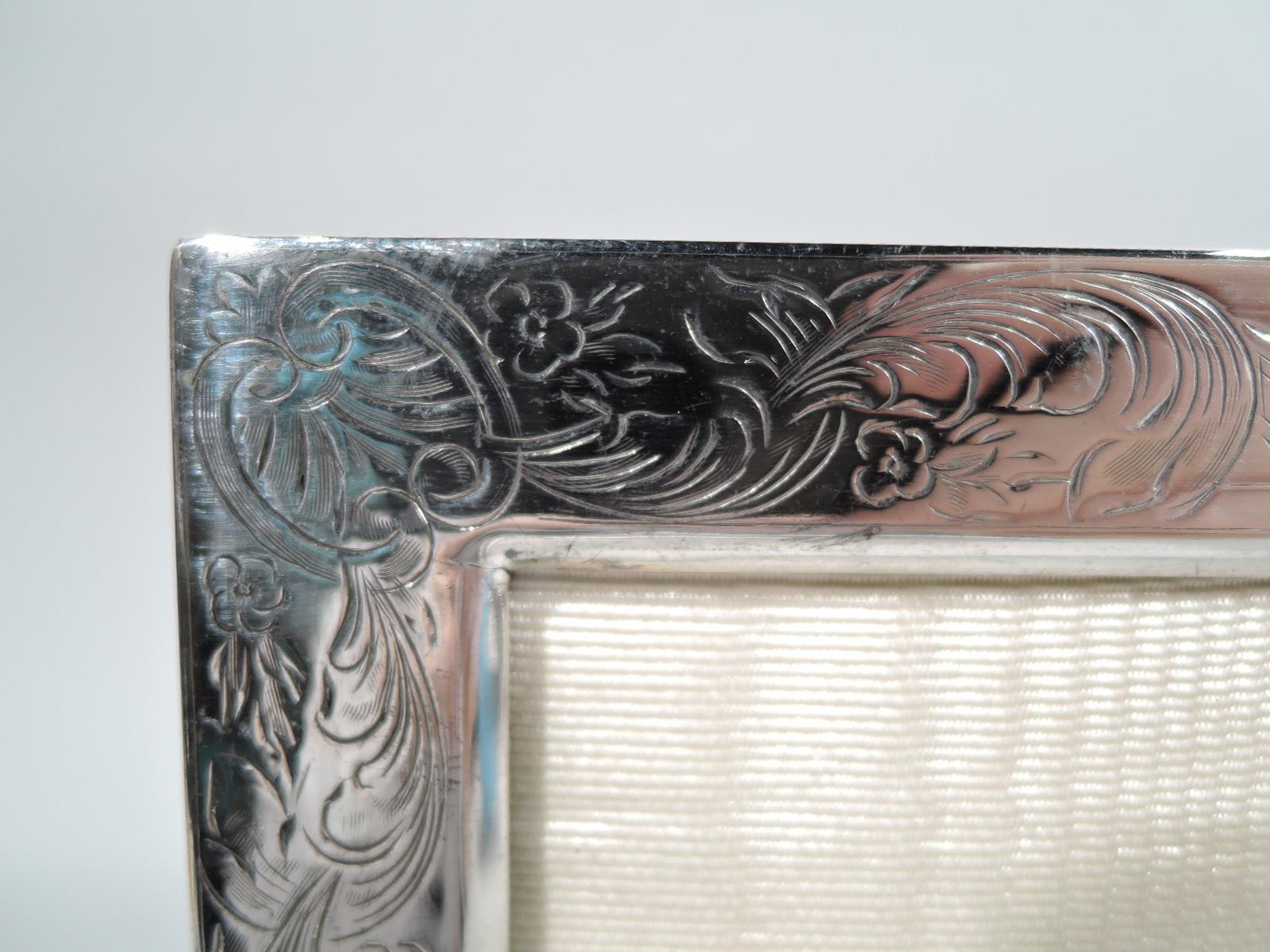 American Edwardian Art Nouveau sterling silver picture frame, circa 1910. Rectangular window in flat surround with engraved scrolling leaves and flowers at corners. With glass, silk lining, and velvet back and hinged support for portrait (vertical)