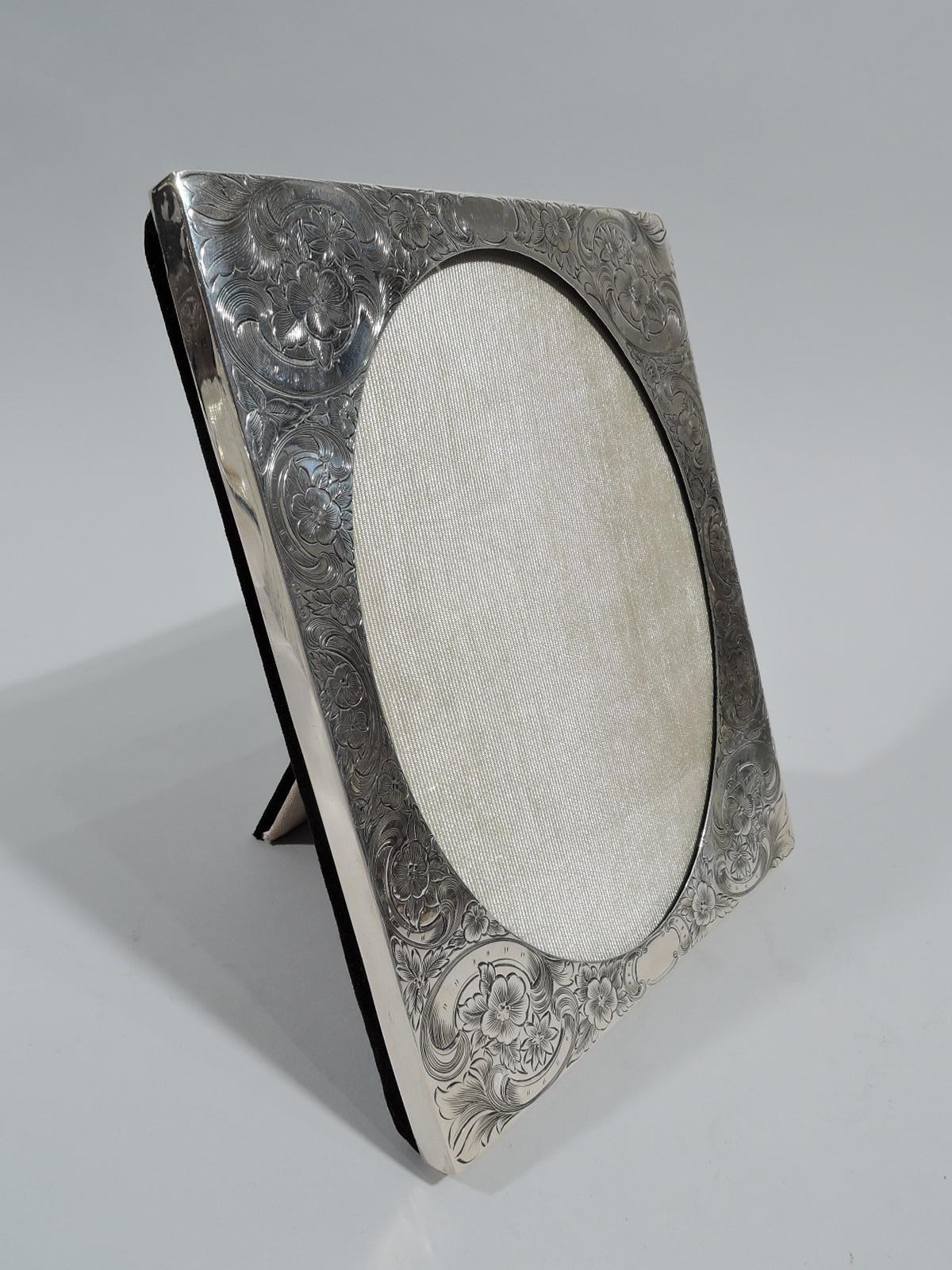 American Edwardian Art Nouveau sterling silver picture frame, ca 1910. Oval window in rectangular surround engraved with dense flowers and scrolls; sides plain. With glass, silk lining, and velvet back and hinged easel support for portrait