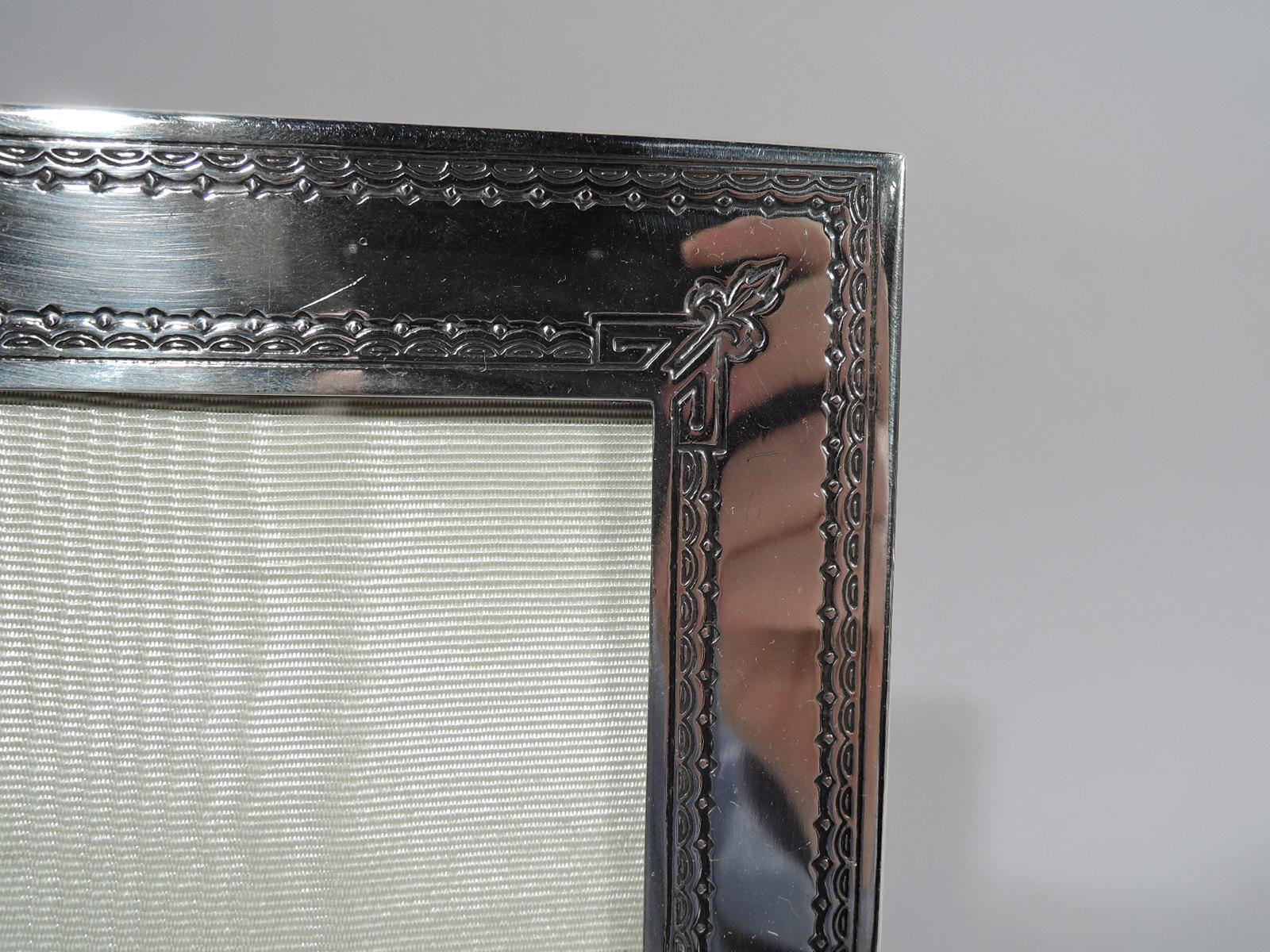 Edwardian classical engraved and acid-etched sterling silver picture frame. Rectangular window in flat surround with rosette rondels on sides and leaf in trapezoid on bottom rail. Top rail has inverted trapezoid (vacant). Ornamental borders and