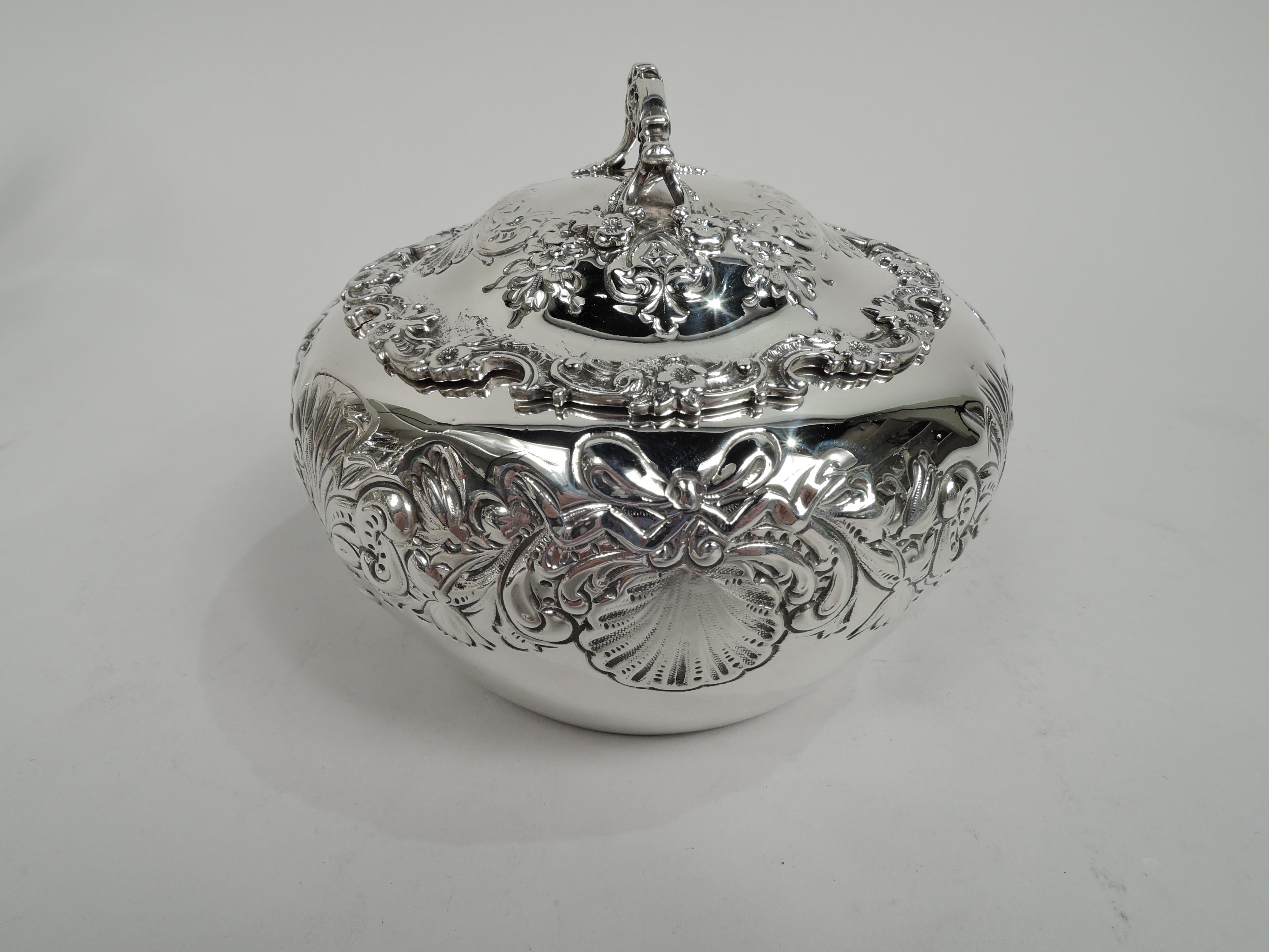 Turn-of-the-century Edwardian Classical sterling silver trinket box. Made by William B. Durgin Co. (later part of Gorham) in Concord. Round with curved and tapering sides. Cover domed with applied flower and scroll rim; scroll bracket handle same.