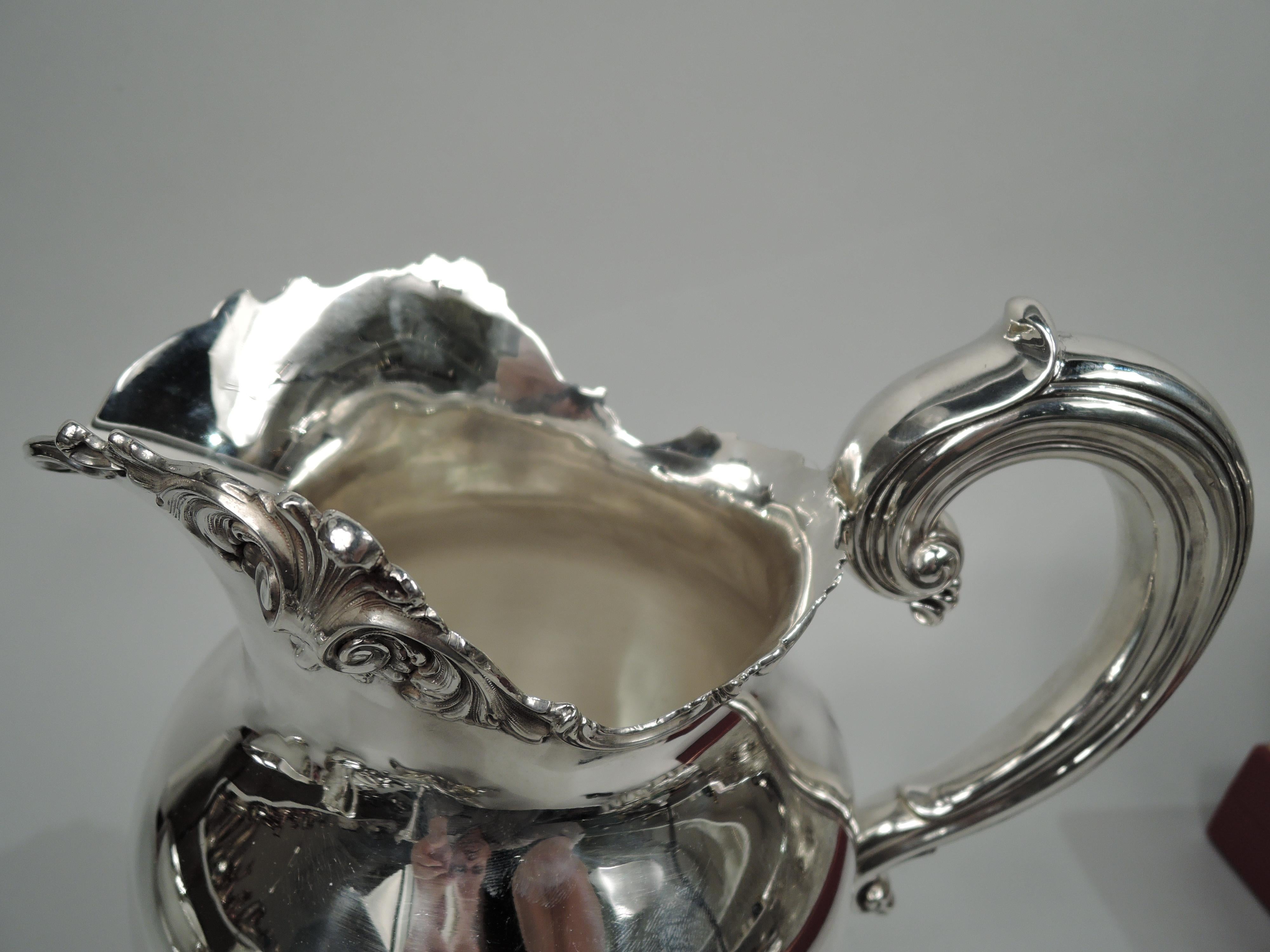 Edwardian Classical sterling silver water pitcher. Made by Frank W. Smith in Gardner, Mass., ca 1910. Full-bodied globular bowl on domed foot; reeded and capped high-looping handle and wide u-spout. Irregular and scrolling rims applied with leafing
