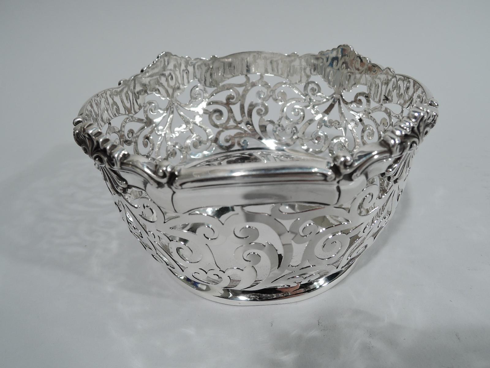 American Edwardian sterling silver wine bottle coaster, circa 1910. Round solid well. Sides have pierced scrollwork and molded rim with applied leafing scallop shells. Solid and skirted foot. Perfect for the intimate one-bottle night. Fully marked