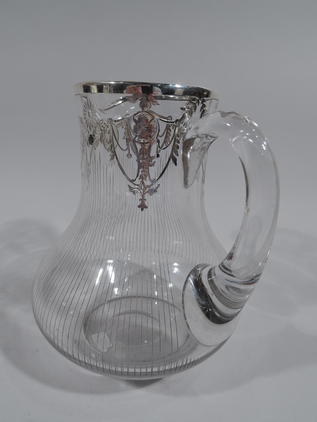 Edwardian Regency glass water pitcher with silver overlay, circa 1910. Bellied baluster with small lip spout and C-scroll handle. At mouth silver overlay garland with pendant flowers and cut paterae. Oval frame with interlaced script monogram. Body