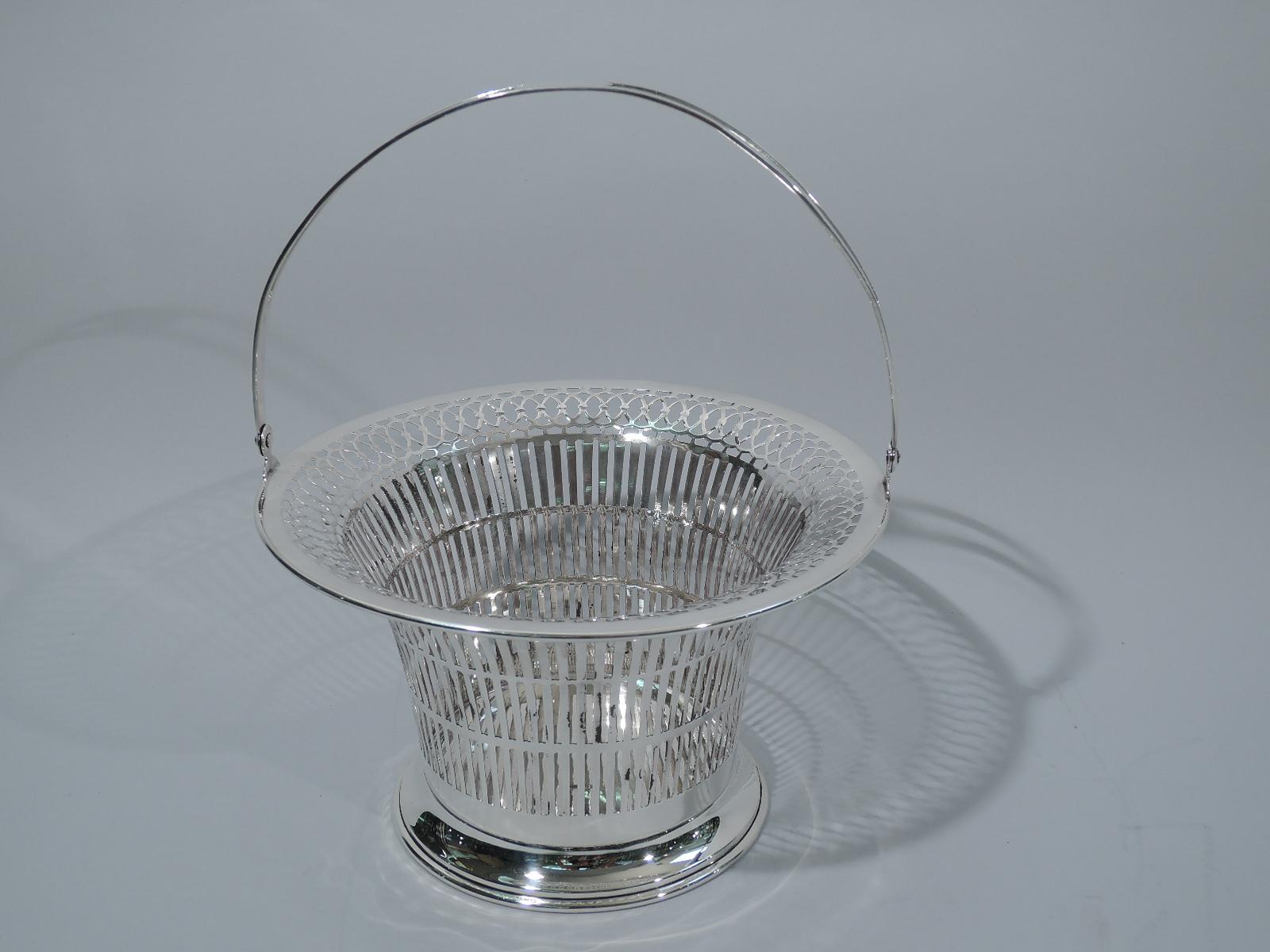 Edwardian sterling silver bucket basket. Made by Meriden Britannia (part of International) in Meriden, Conn., circa 1915. Solid well and spread foot, flared rim, and open tapering c-scroll swing handle with tubular cartouche (vacant). Pierced lines