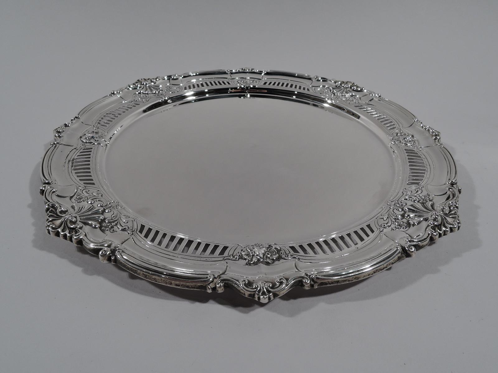 Turn-of-the-century American Edwardian sterling silver cake plate. Round and plain well bordered by linear piercing and applied and chased flowers and scrolls. Rim scrolled and applied with scallop shells. Pretty with a nice size and heft for
