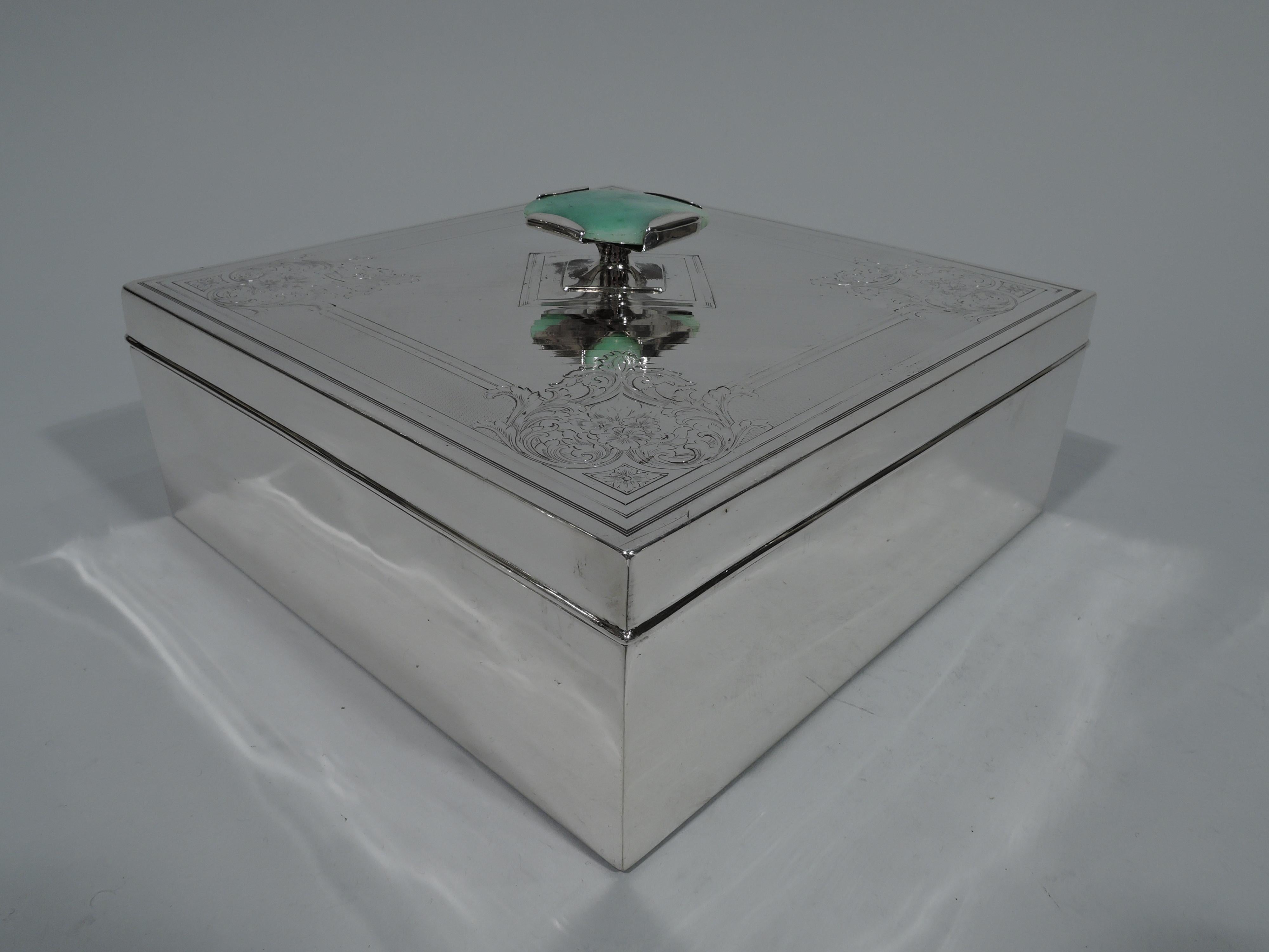 Edwardian sterling silver keepsake box. Square with straight sides and sharp corners. Cover flat with engine-turned ornament, diagonal lines bordered by dense waving. Corners have engraved scrolls and flowers. Mottled green agate finial. Fully