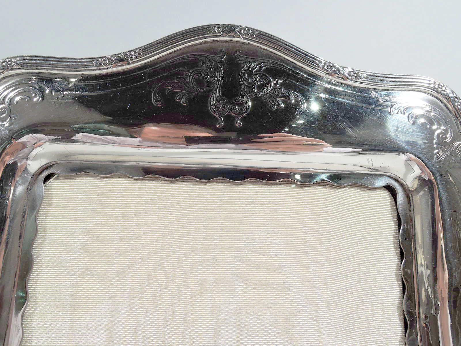 Dulce marco eduardiano americano de plata de ley, hacia 1910. Ventana rectangular con borde festoneado y marco perfilado con lados cóncavos y parte inferior arqueada, y esquinas de doble roleo. Decoración de hojas y conchas grabada al ácido. Borde