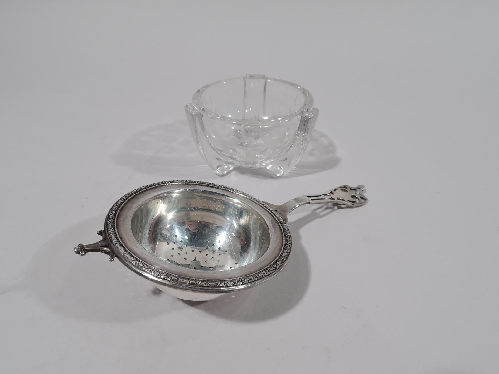 Edwardian sterling silver tea strainer. Made by Watson Company in Attleboro, ca 1920. Strainer: Round bowl with ornamental piercing; rim flat with leaf and guilloche border. Handle open with armorial terminal. Fully marked and numbered W49.