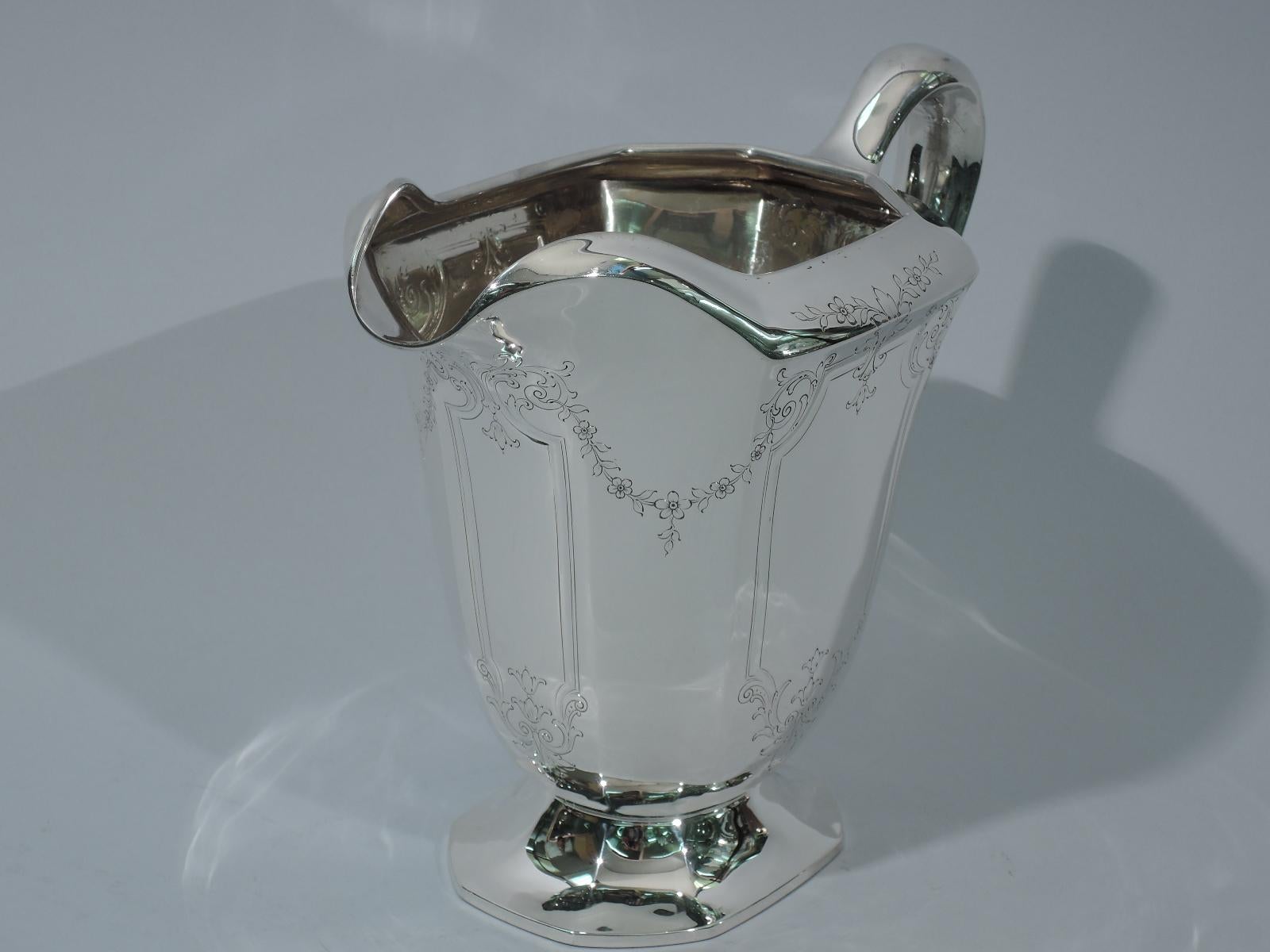 Edwardian sterling silver water pitcher. Made by Graff, Washbourne & Dunn in New York. Chamfered rectilinear body and foot, and scrolled handle. Engraved ornament: Curvilinear frames with scrolls and foliage linked by floral garlands. Hallmark