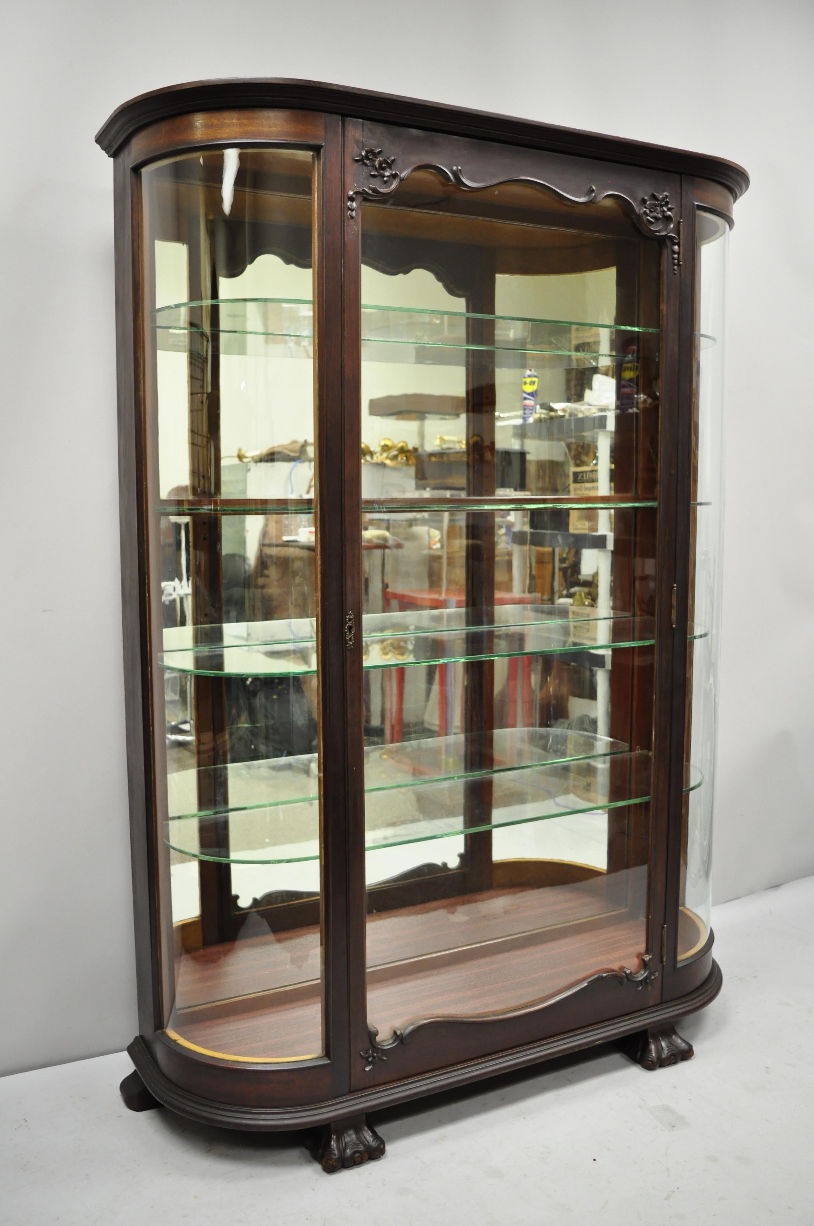 Antique American Empire bow glass carved mahogany claw foot china cabinet. Item features 2 bowed glass panels, mirror back, paw feet, mahogany wood frame, nicely carved details, no key, but unlocked, 4 adjustable glass shelves, very nice antique