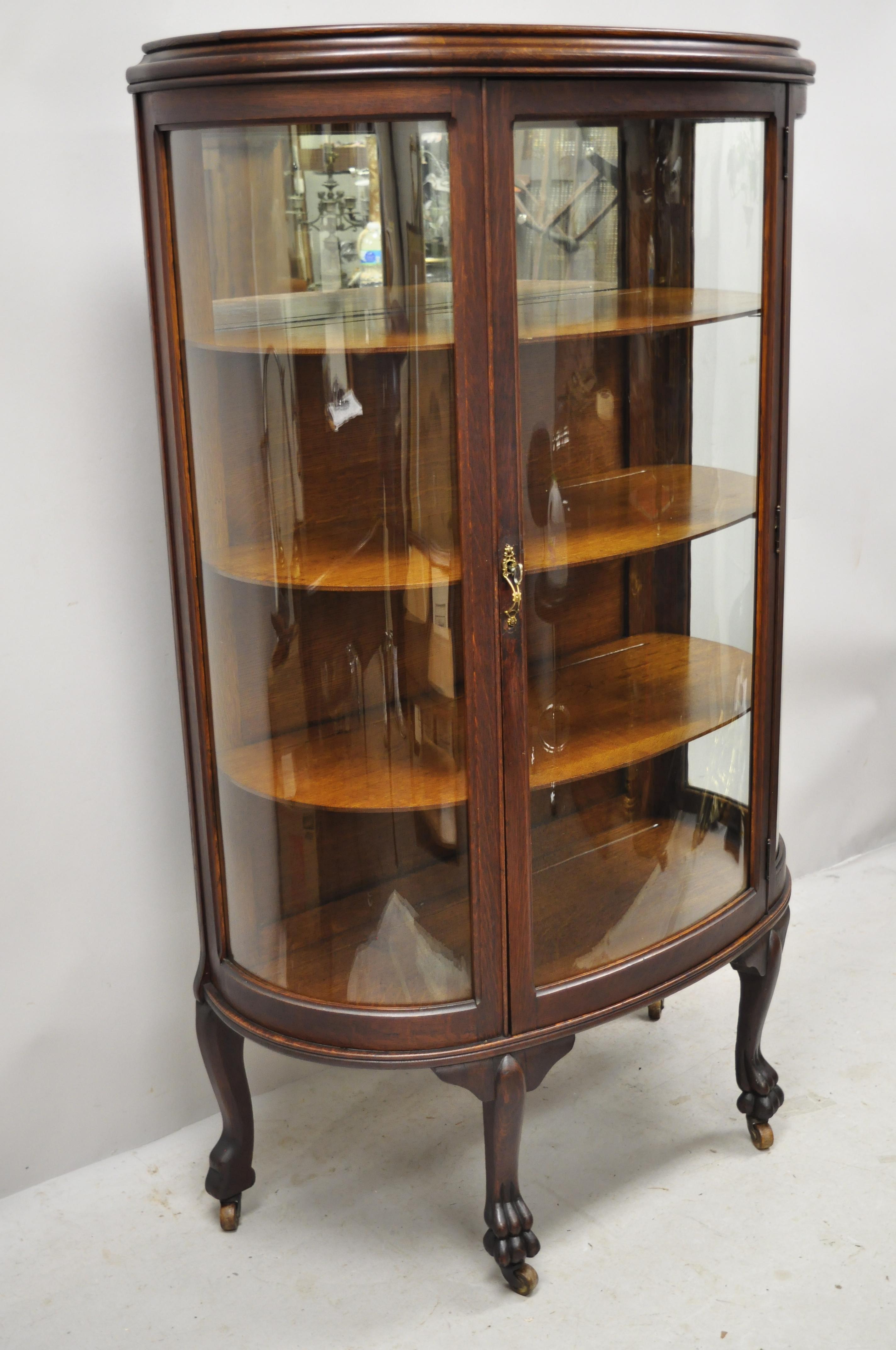 Antique American Empire bow glass oak paw feet mirror back China cabinet curio. Item features 3 curved/bowed glass panes, paw feet, rolling casters, beautiful wood grain, 3 wooden shelves, very nice antique item, circa early 1900s. Measurements: