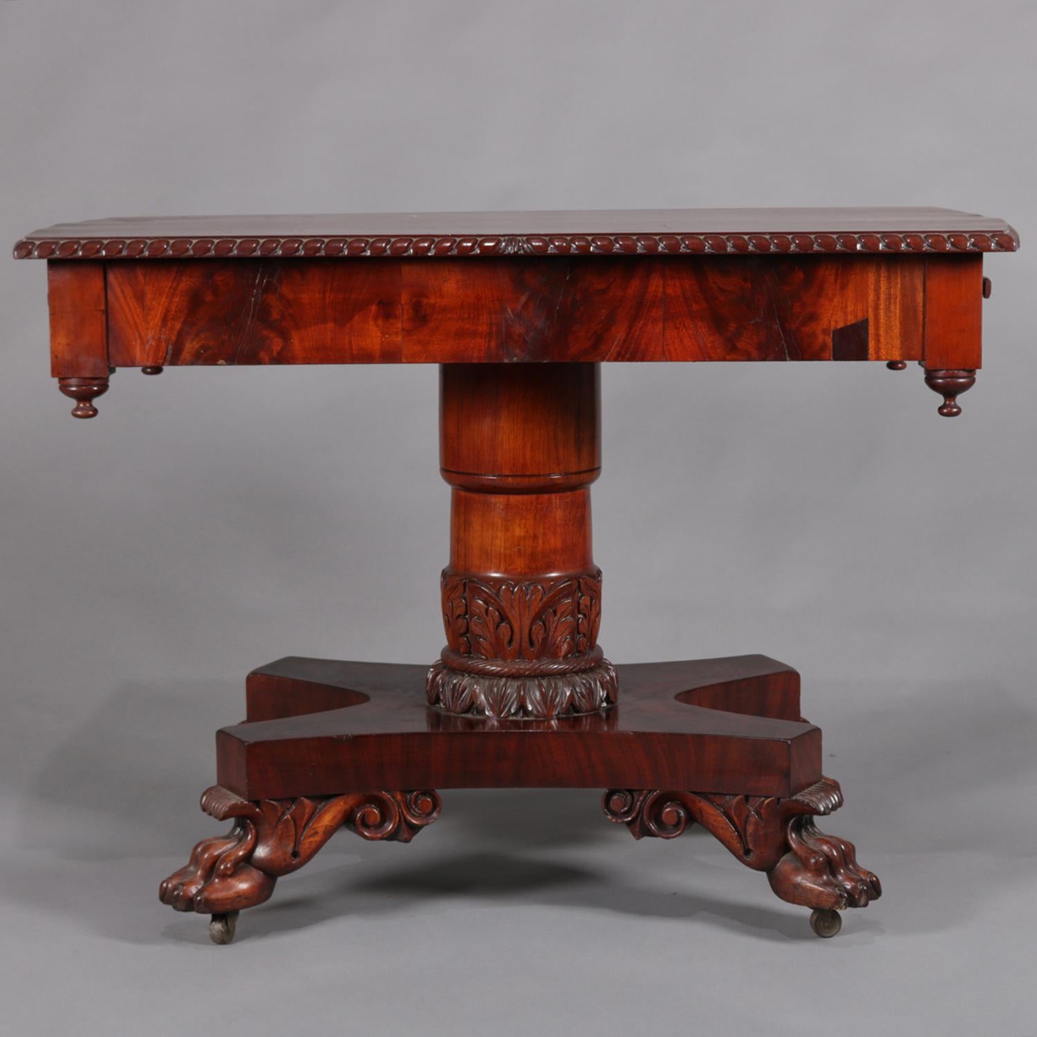 Antique American Empire console table features flame mahogany construction with top bordered in carved rope twist over case with two drawers and four drop corner finials, pedestal with carved foliate acanthus collar on base raised on carved paw feet